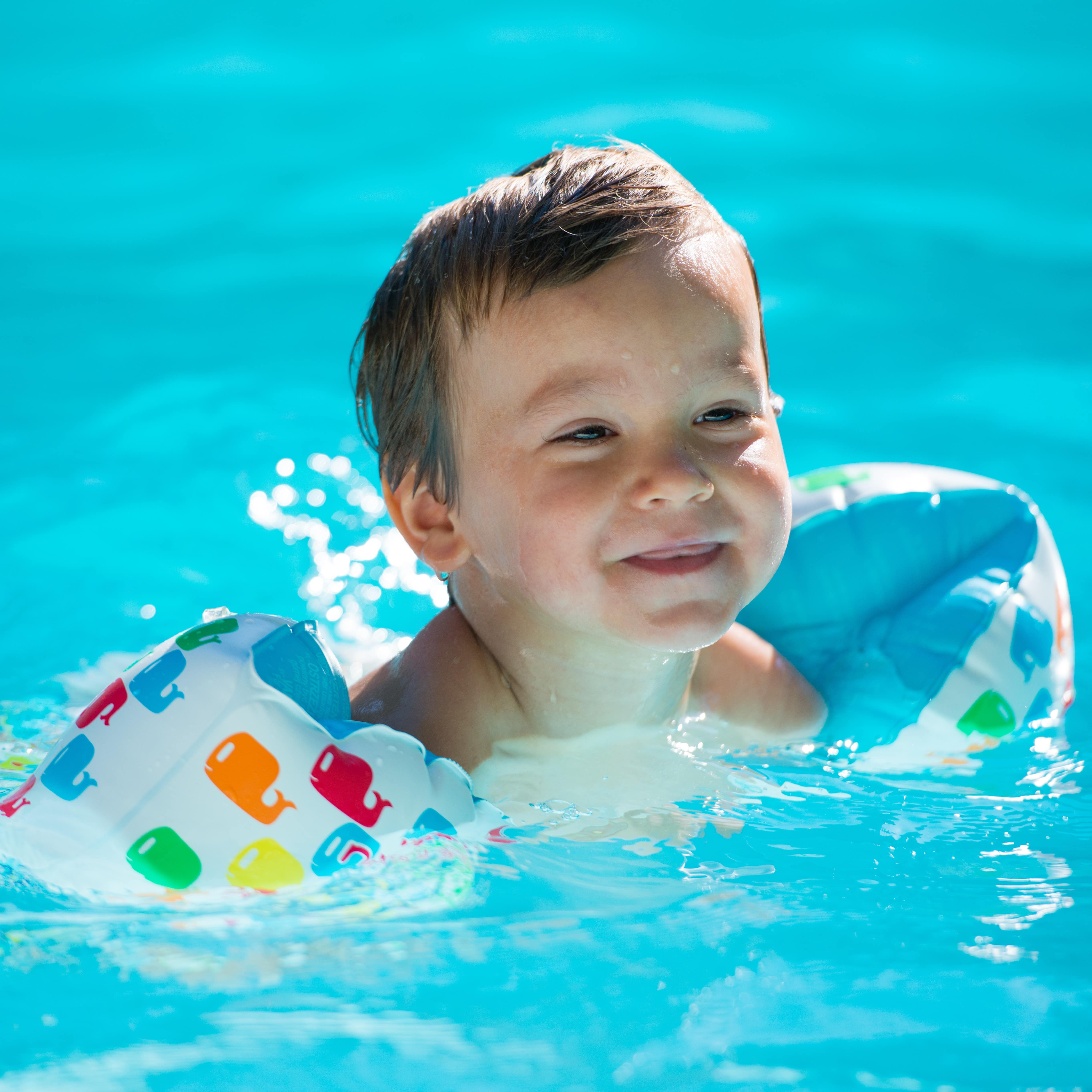 Kleiner Junge mit weiß-bunten Schwimmflügeln in einem Pool.