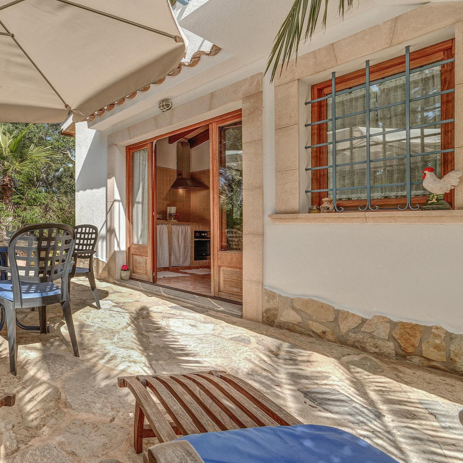 Ferienwohnung in Cala Ratjada mit großer Terrasse, darauf ein Tisch, Stühle und Liegestühle mit Blick ins Grüne
