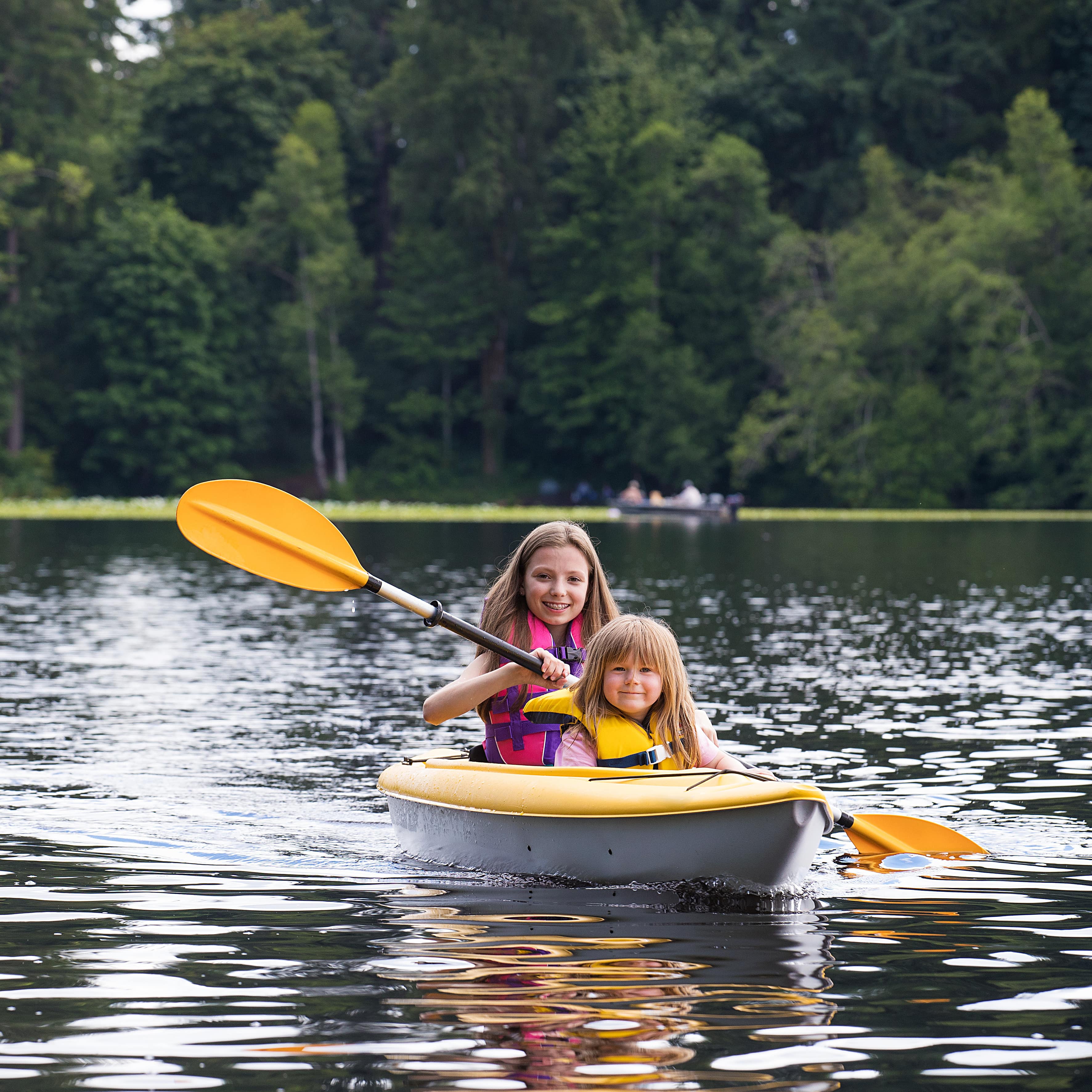 2 Mädchen mit Schwimmwesten in einem Kajak auf einem See.