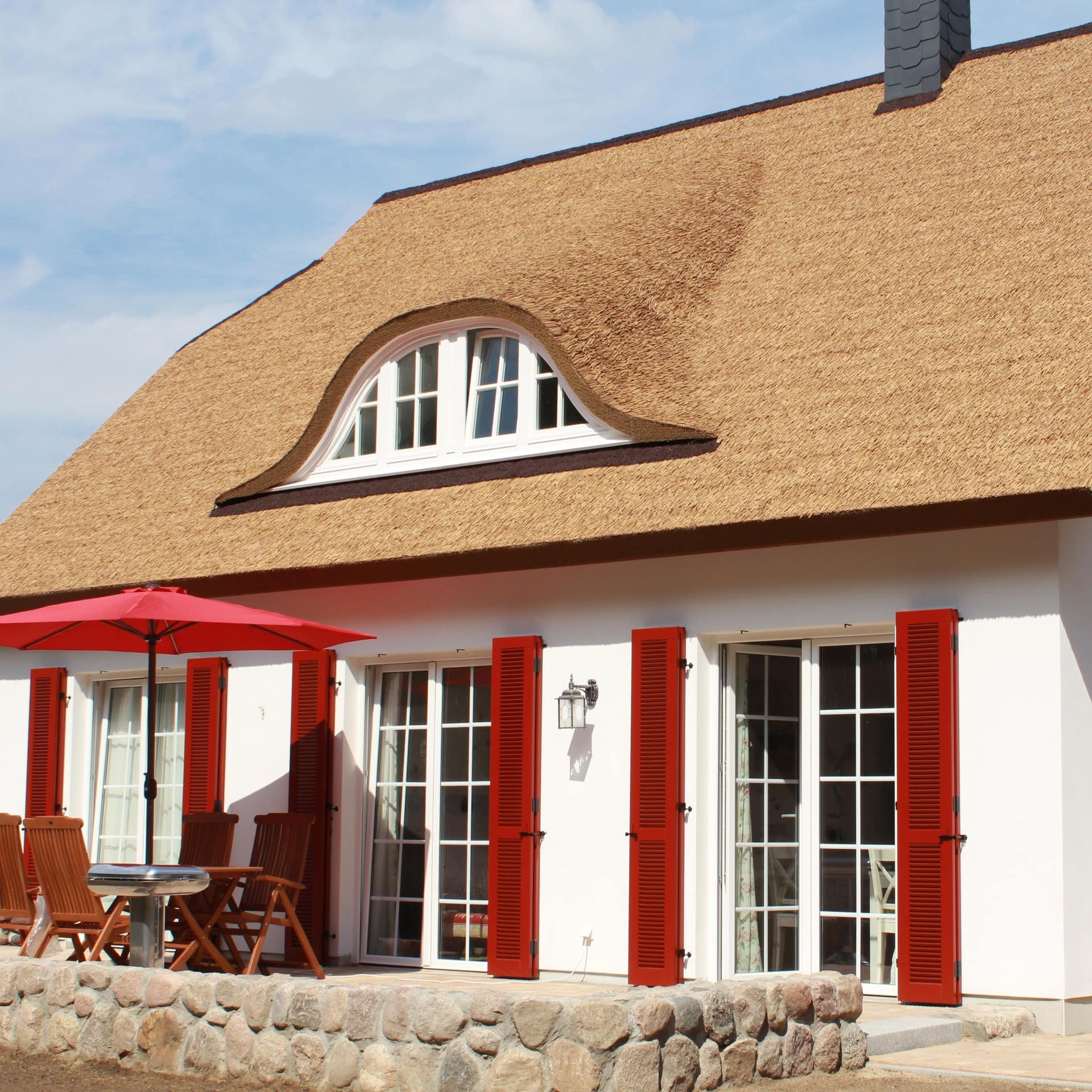 Ein weißes Ferienhaus am Kölpinsee mit Reetdach und roten Fensterläden sowie Terrasse
