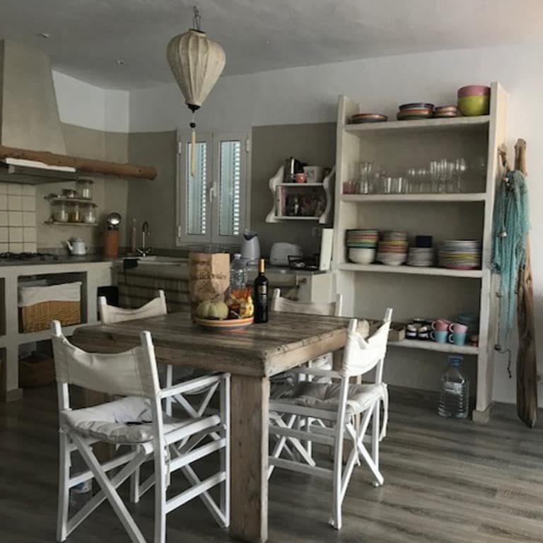 Ferienwohnung auf Ibiza mit gemütlich eingerichteter Küche, darin ein Esstisch mit vier hellen Stühlen und ein Korbsessel