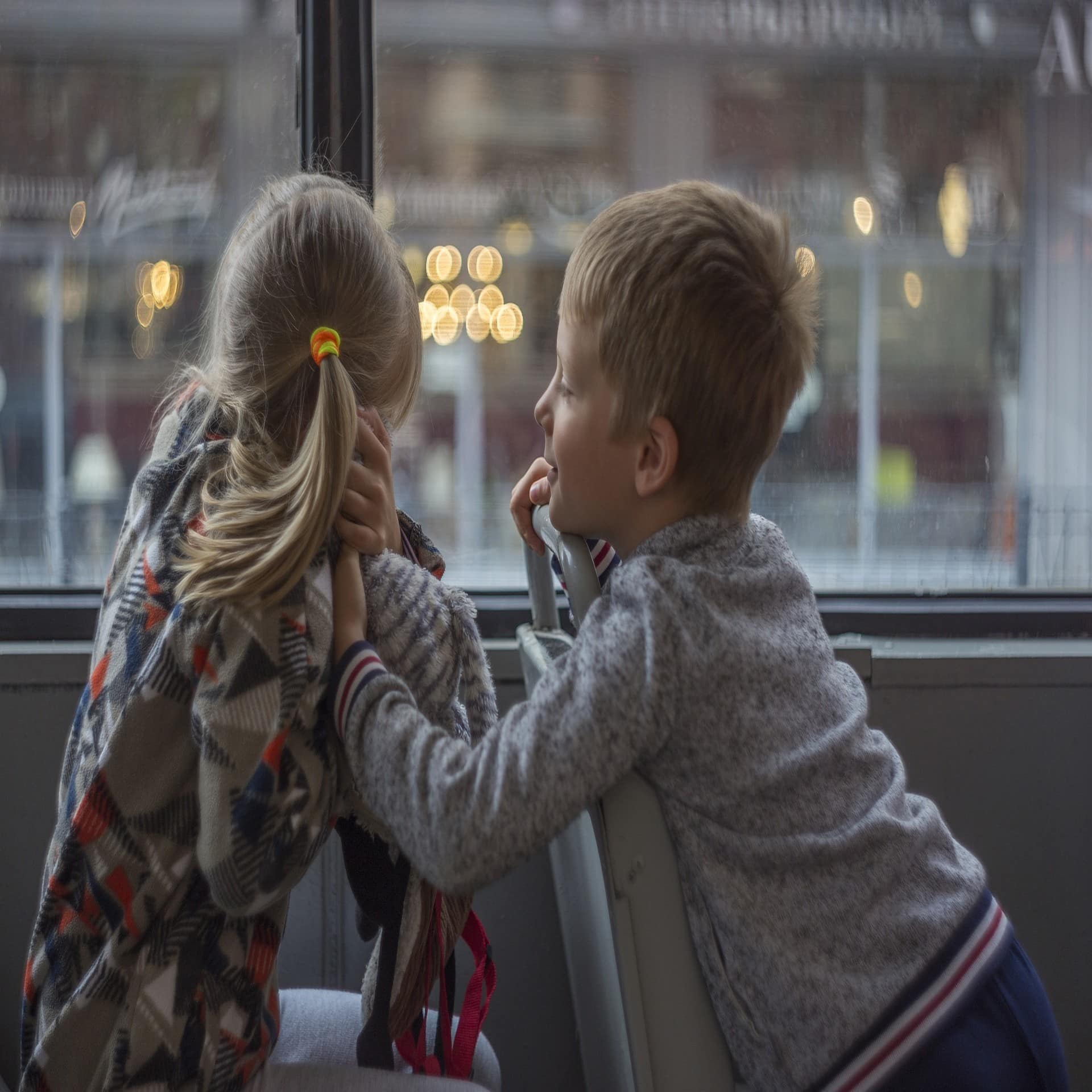 Ein Junge und ein Mädchen sitzen hintereinander in einem Bus. Der Junge dreht sich zum Mädchen um. 