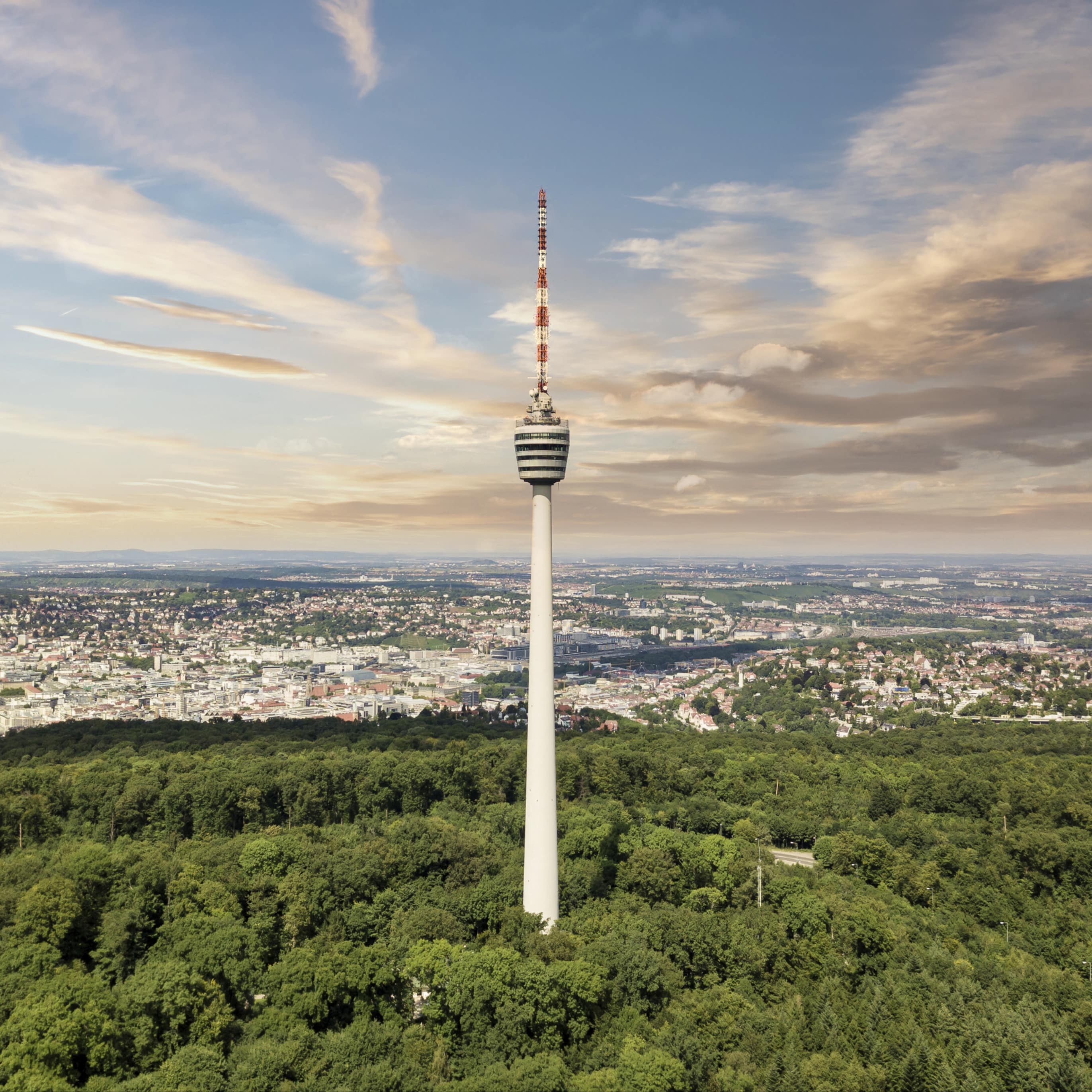 Panoramablick: Der Stuttgarter Fernsehturm, umgeben von Wald, dahinter die Stadt.