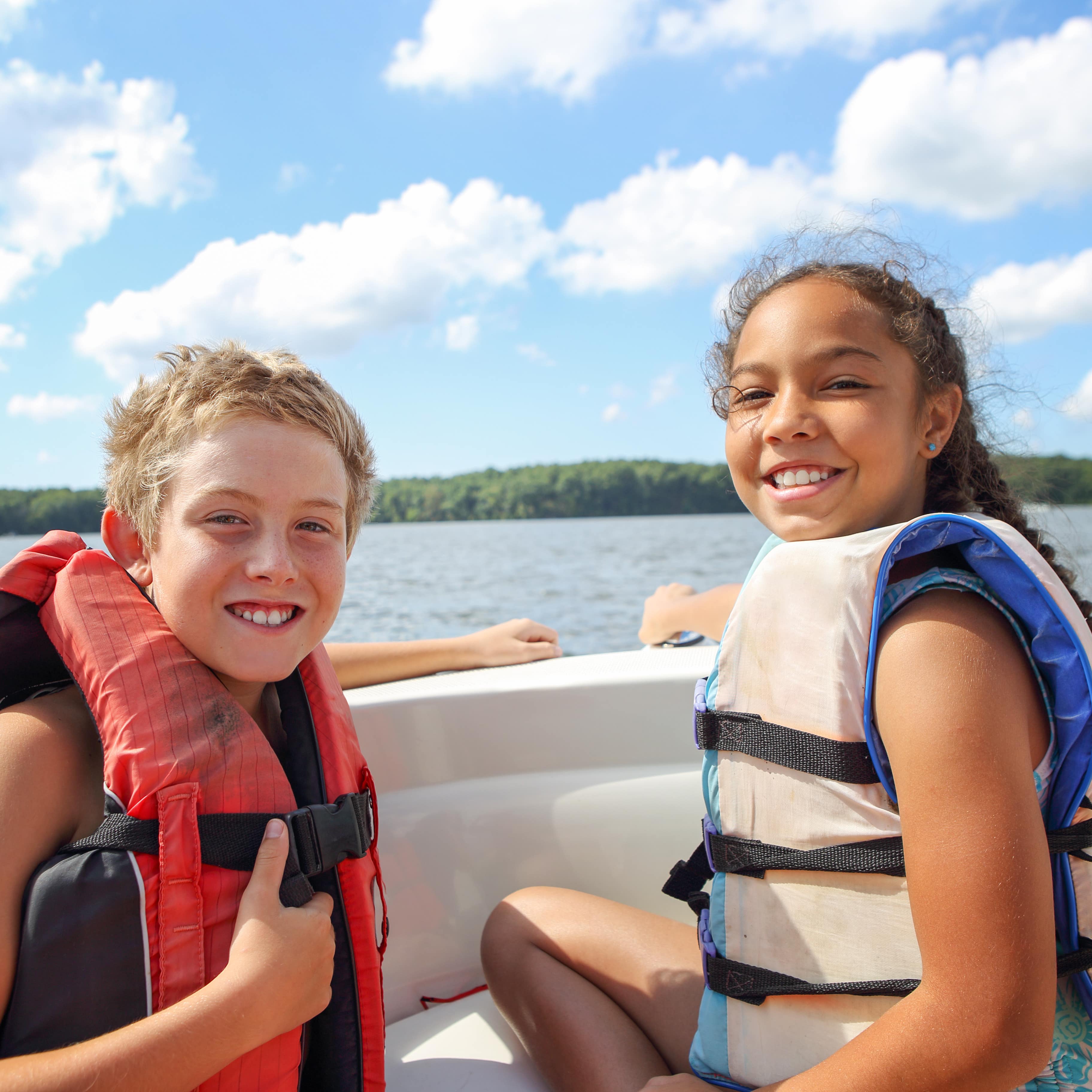 Junge und Mädchen mit Schwimmwesten in einem Boot.