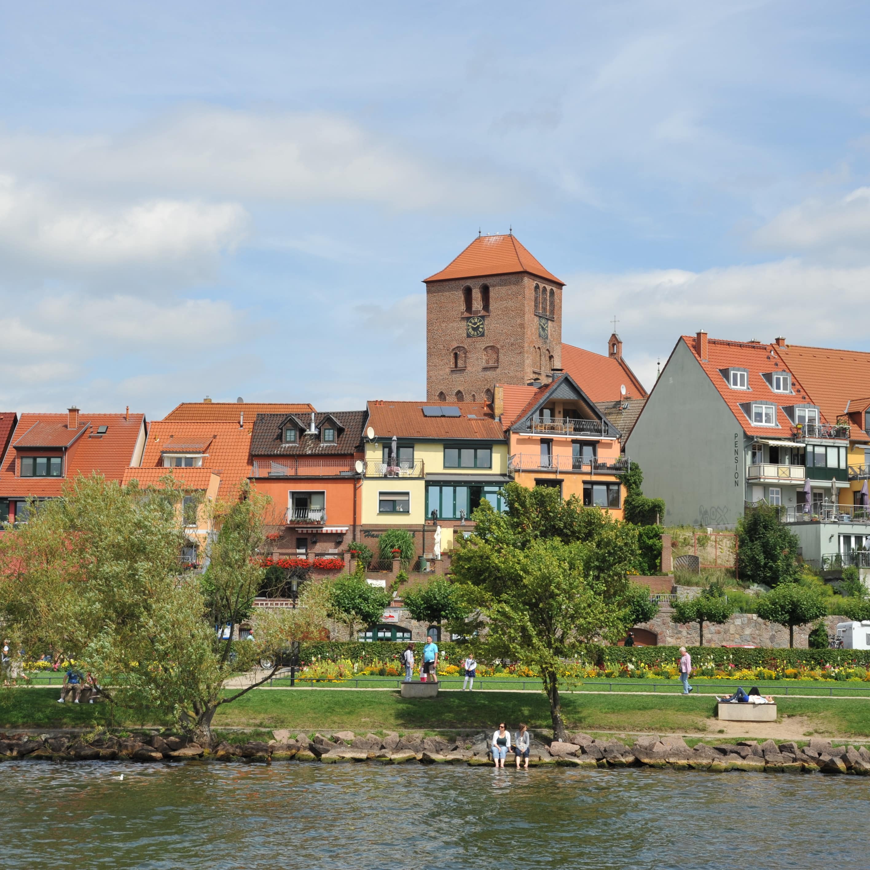 Blick über das Wasser auf die grüne Uferpromenade und Wohnhäuser von Waren.