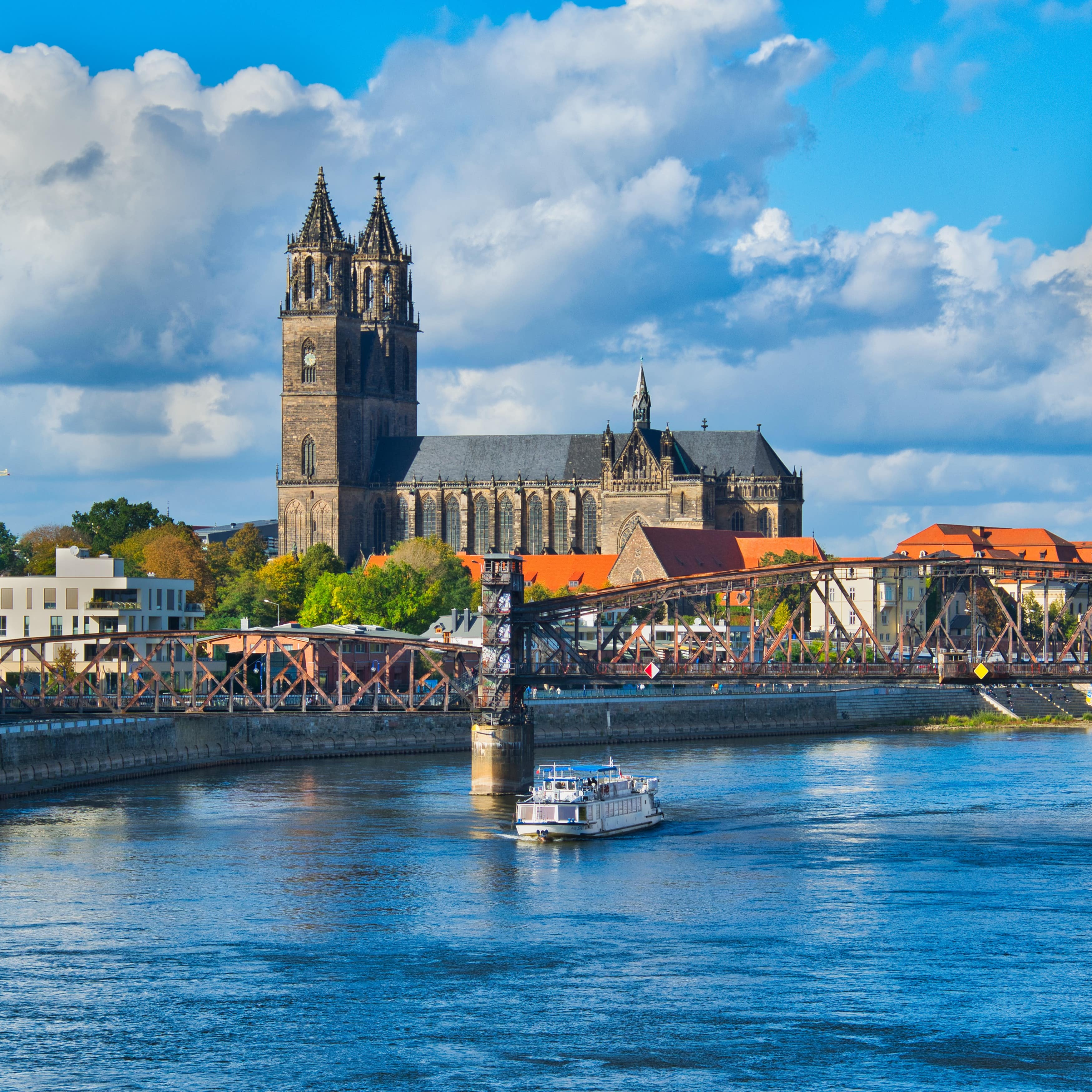 Panoramablick über Magdeburg und die Elbe. Ein Schiff schippert unter einer Brücke hindurch.