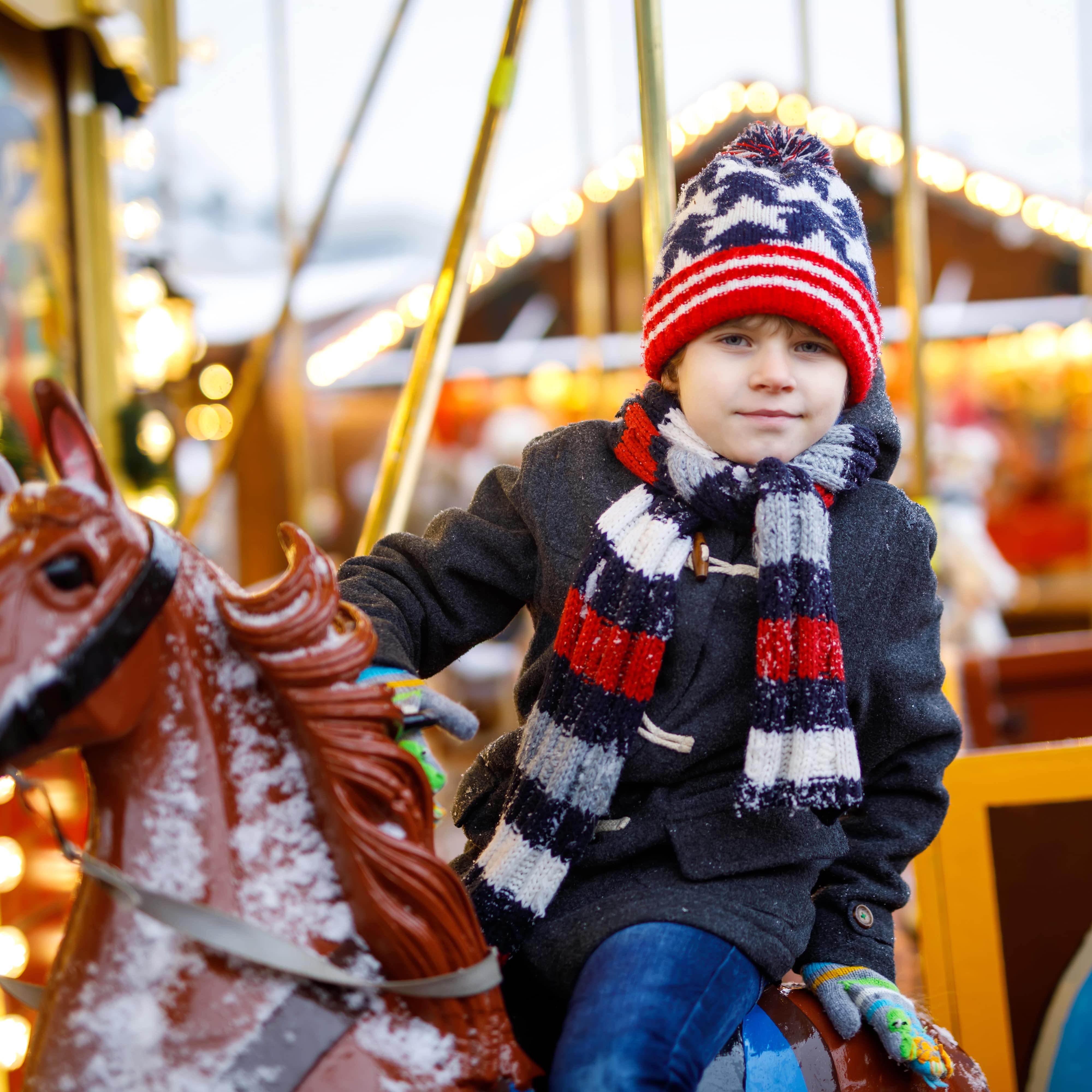 Nahaufnahme: Ein Junge in Winterkleidung auf einem Karussell auf dem Weihnachtsmarkt.