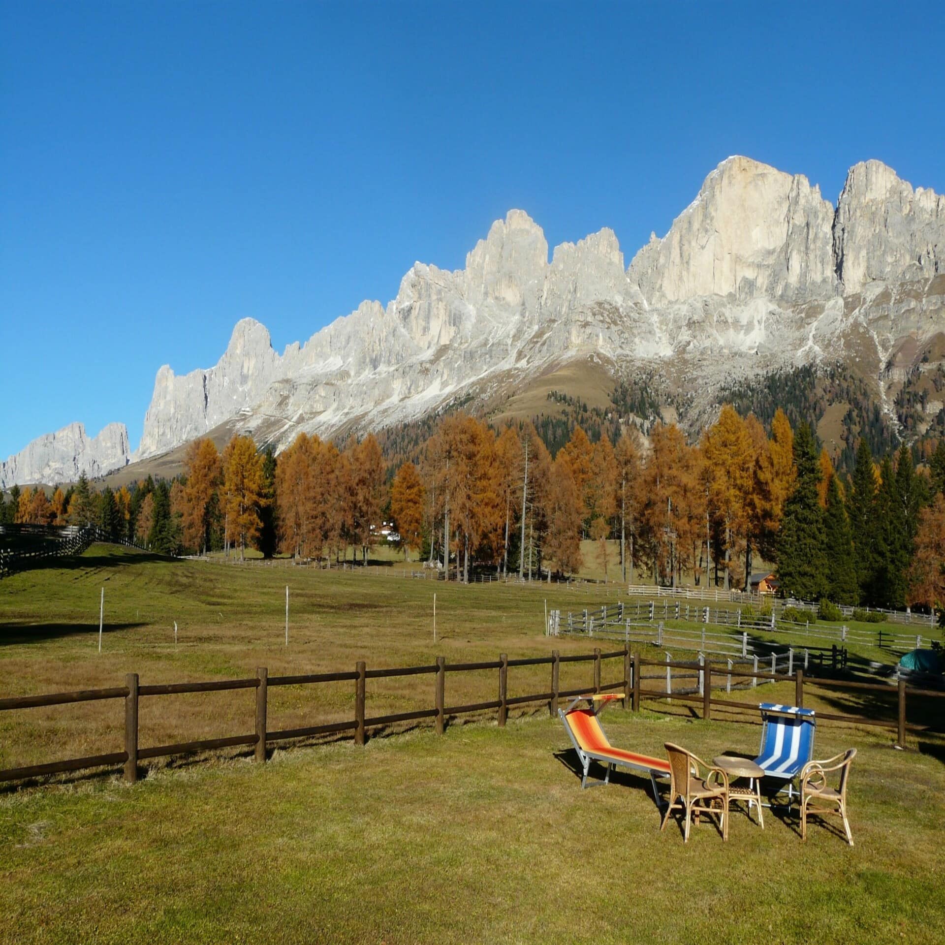 Garten mit Tisch, Stühlen und Liegestühlen sowie Blick auf die Berge Südtirols. Die Sonne scheint, es ist Herbst.