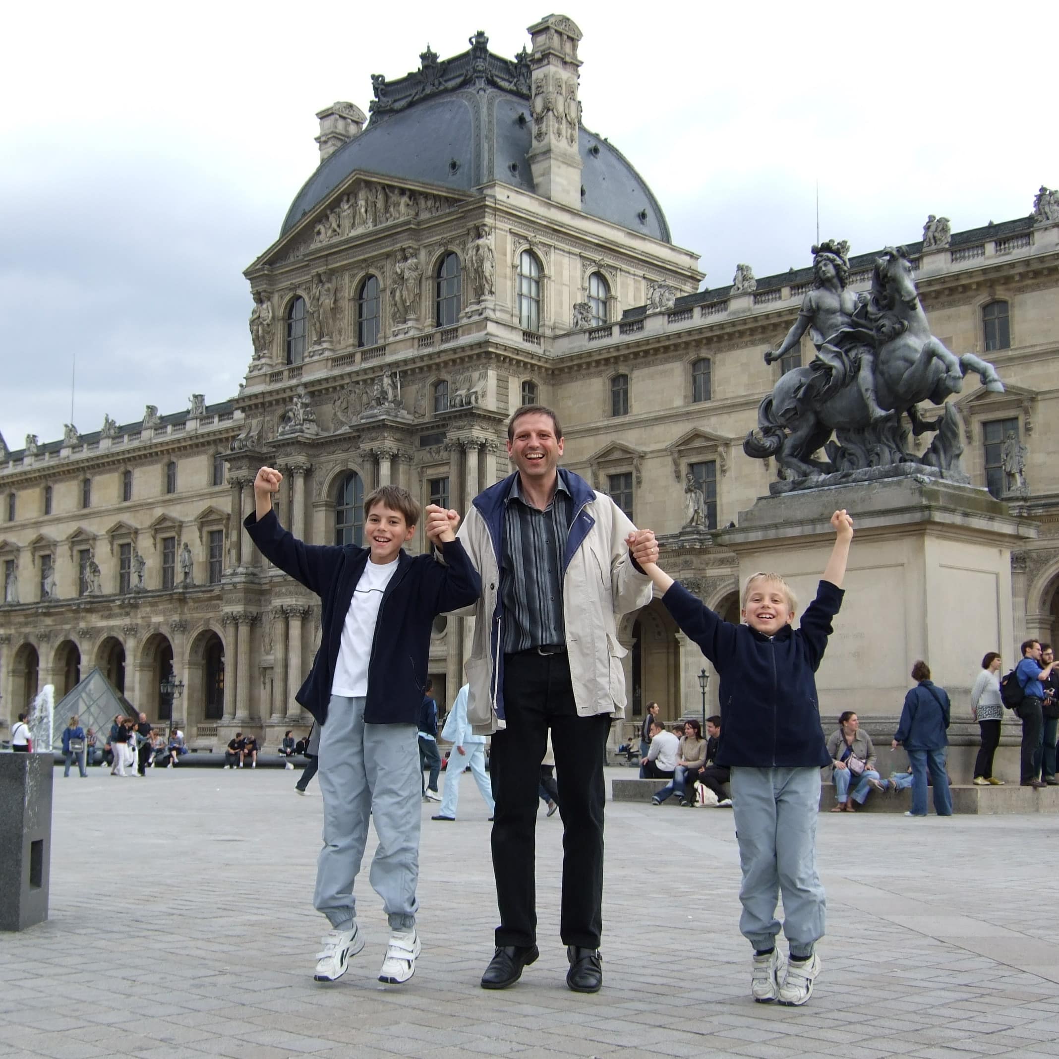 Vater und 2 Söhne hüpfen vor dem Louvre in die Luft.