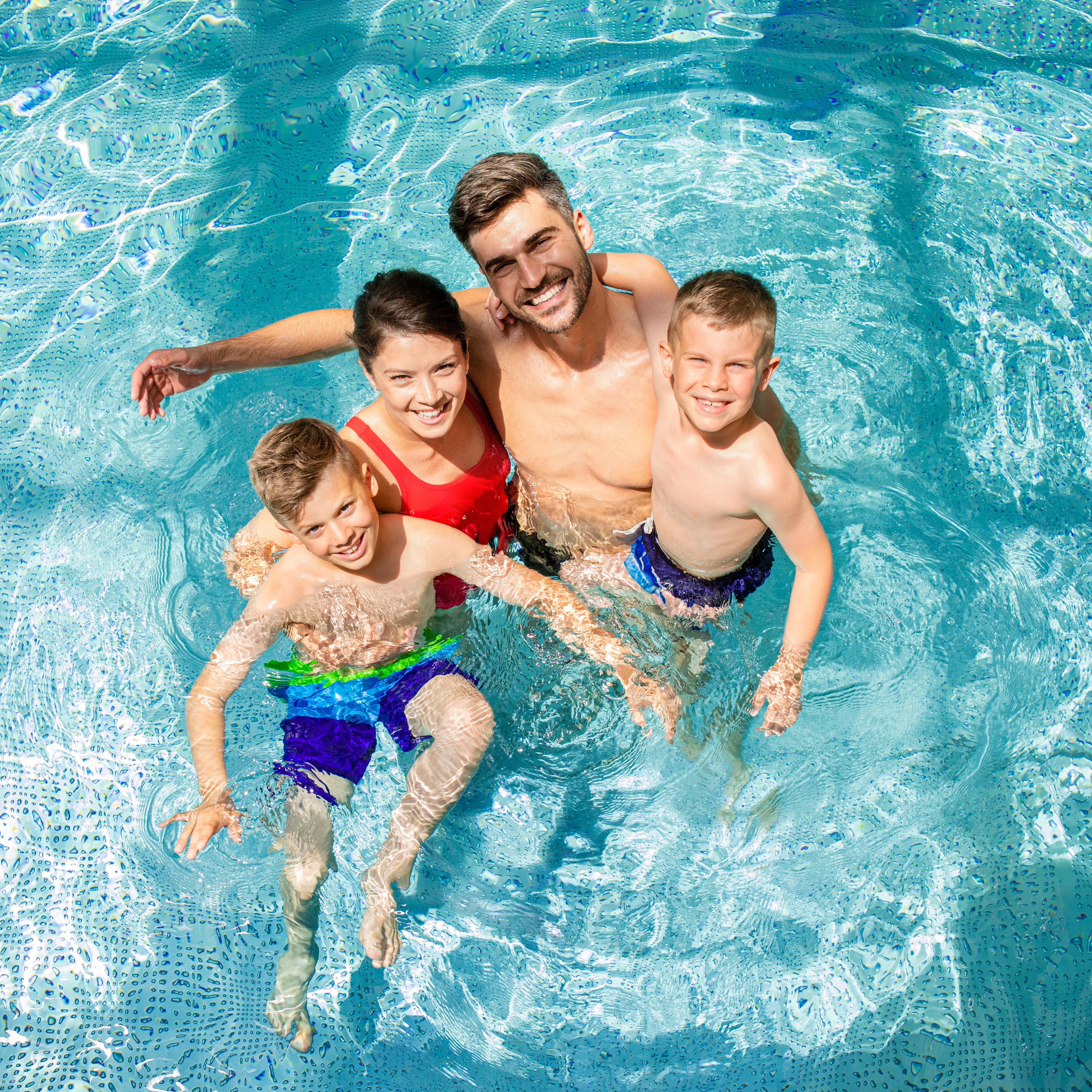 Familie mit 2 Söhnen im Wasser eines Indoor-Pools, alle lachen in die Kamera.