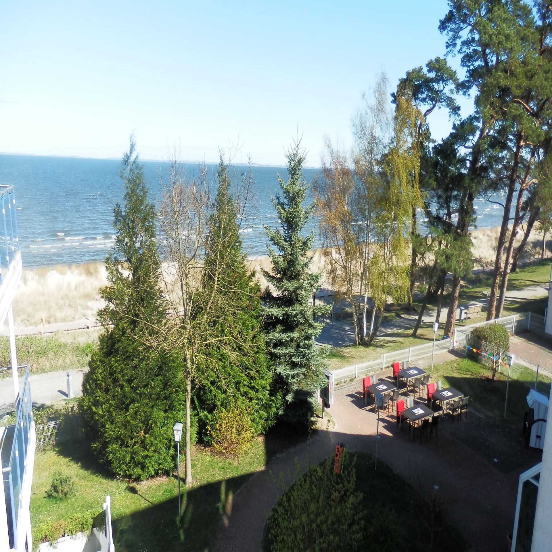 Blick von einem Balkon auf Bäume, den Strand und das Meer. 