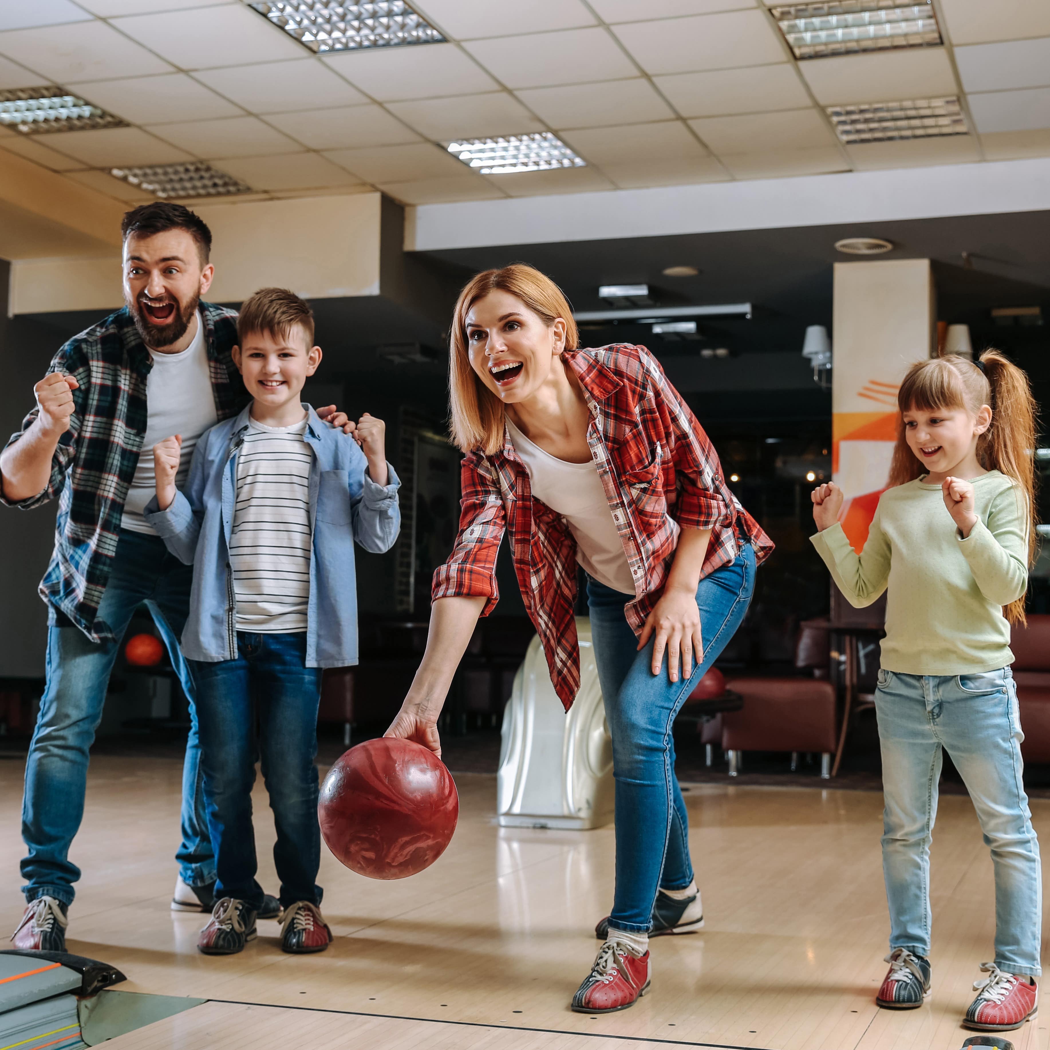 Eltern mit 2 Kindern beim Bowling. Die Mutter schwingt die Kugel.