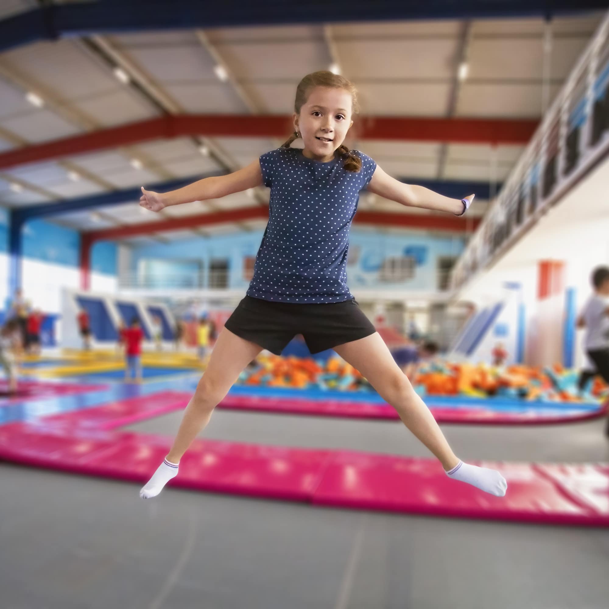 Ein Mädchen in Sommerkleidung und mit Socken in einem Trampolinpark.