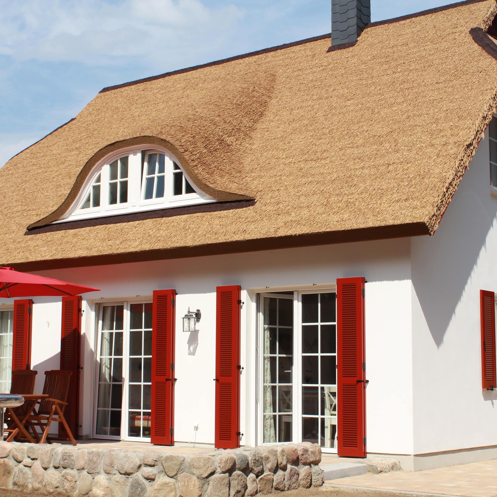 Blick auf ein Haus mit Reetdach und roten Fensterläden in Koserow, in dem sich Ferienwohnungen befinden. 