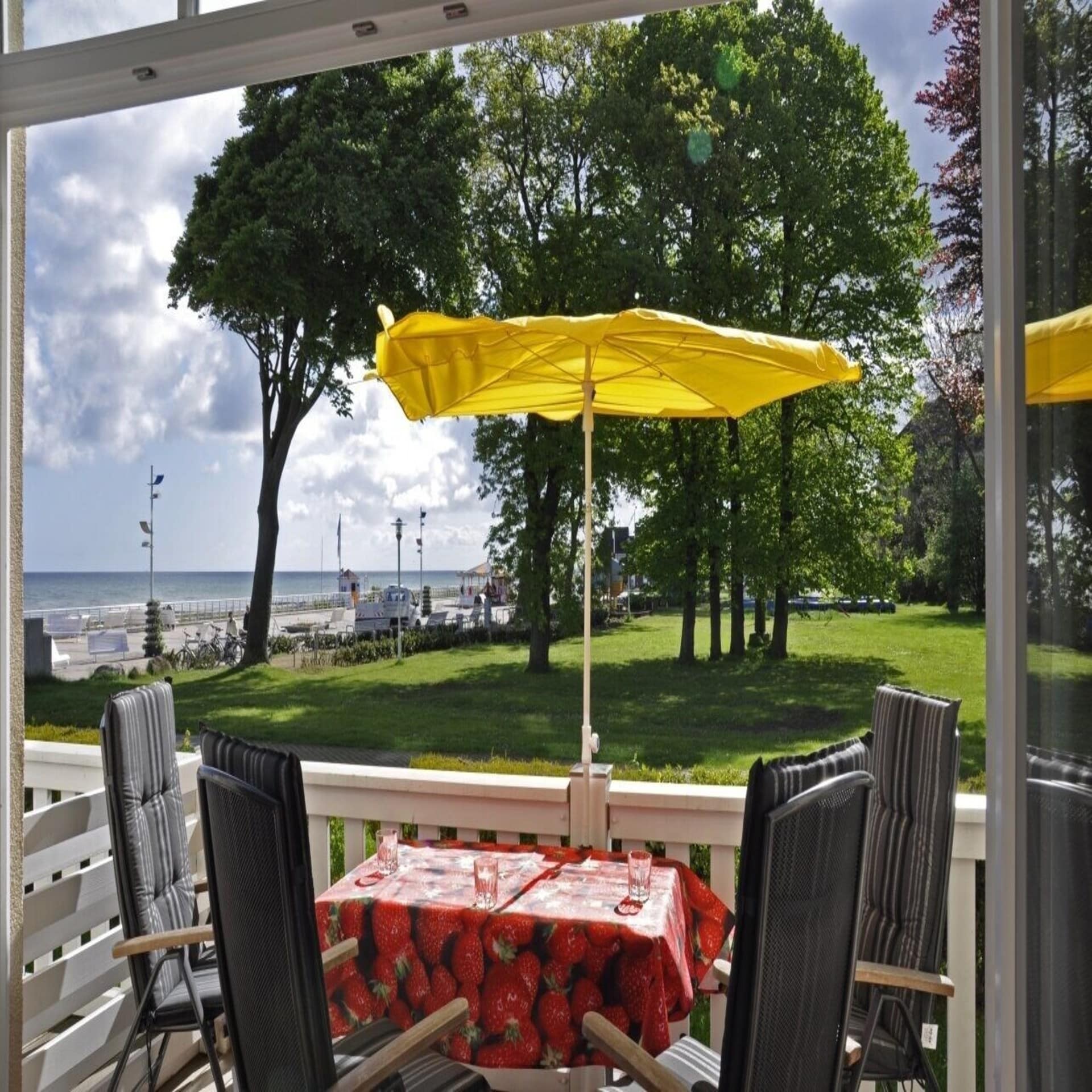 Eine Terrasse mit Stühlen und Sonnenschirm und Blick auf die Ostsee und eine Wiese.
