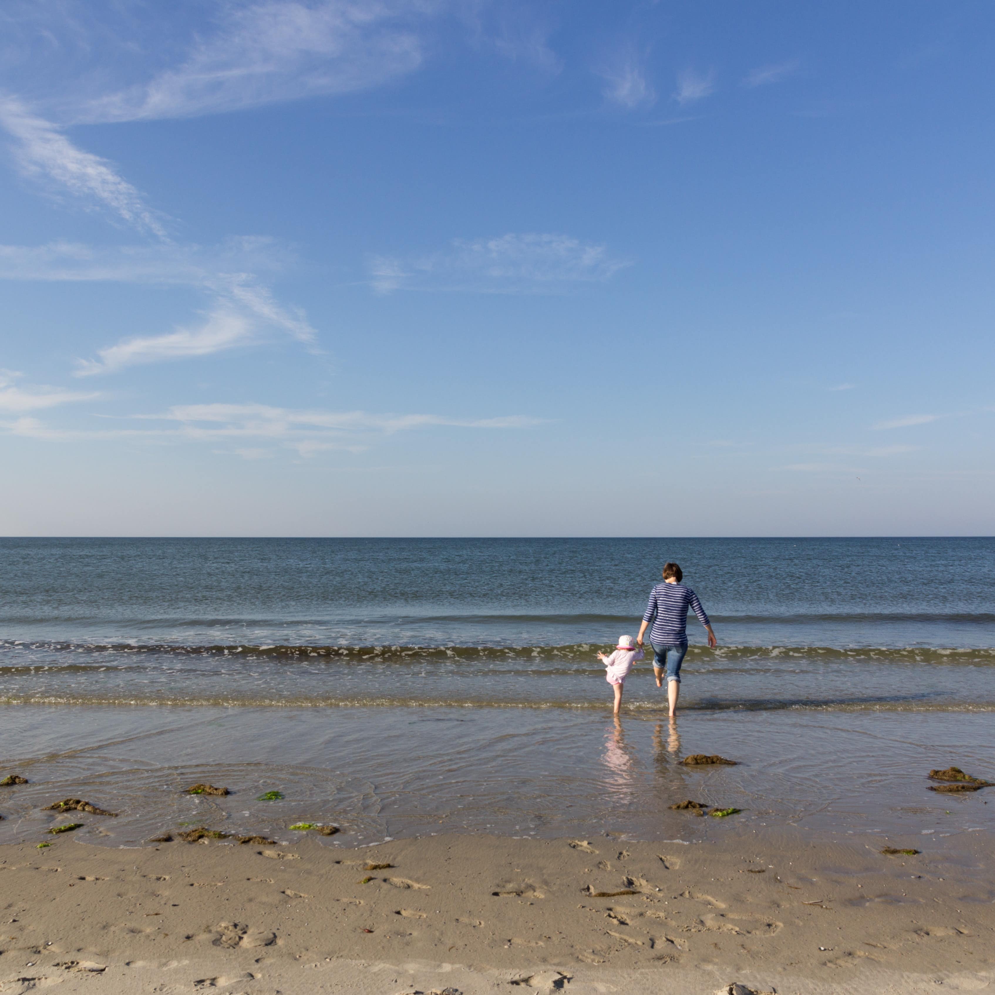 Mutter und Kleinkind mit dem Füßen in Meerwasser.