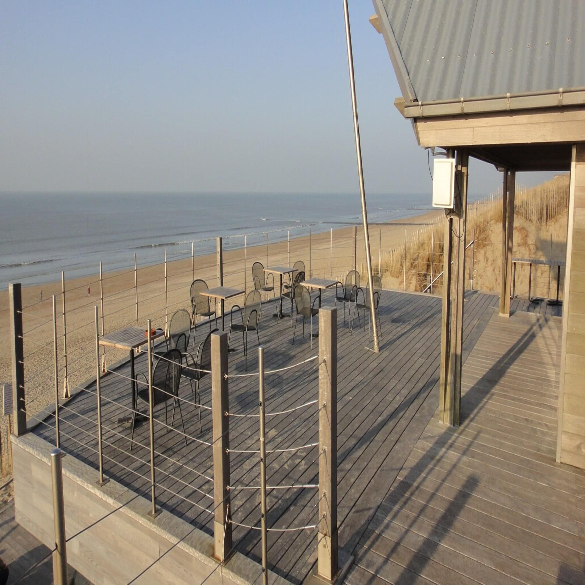 Holzveranda mit Tischen und Stühlen direkt am Strand.