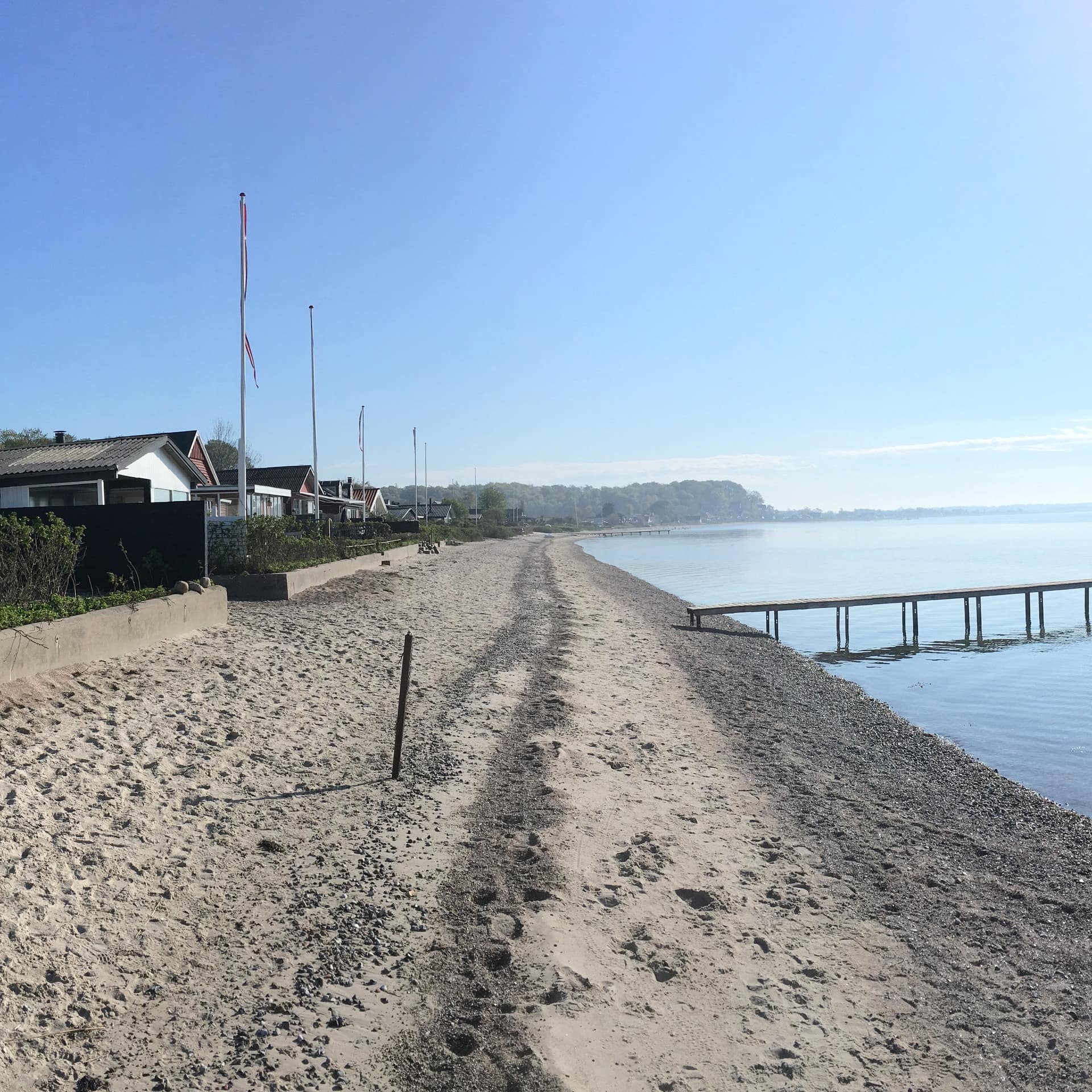 Blick am Strand an der dänischen Nordsee entlang, links liegen Häuser direkt am WasserF