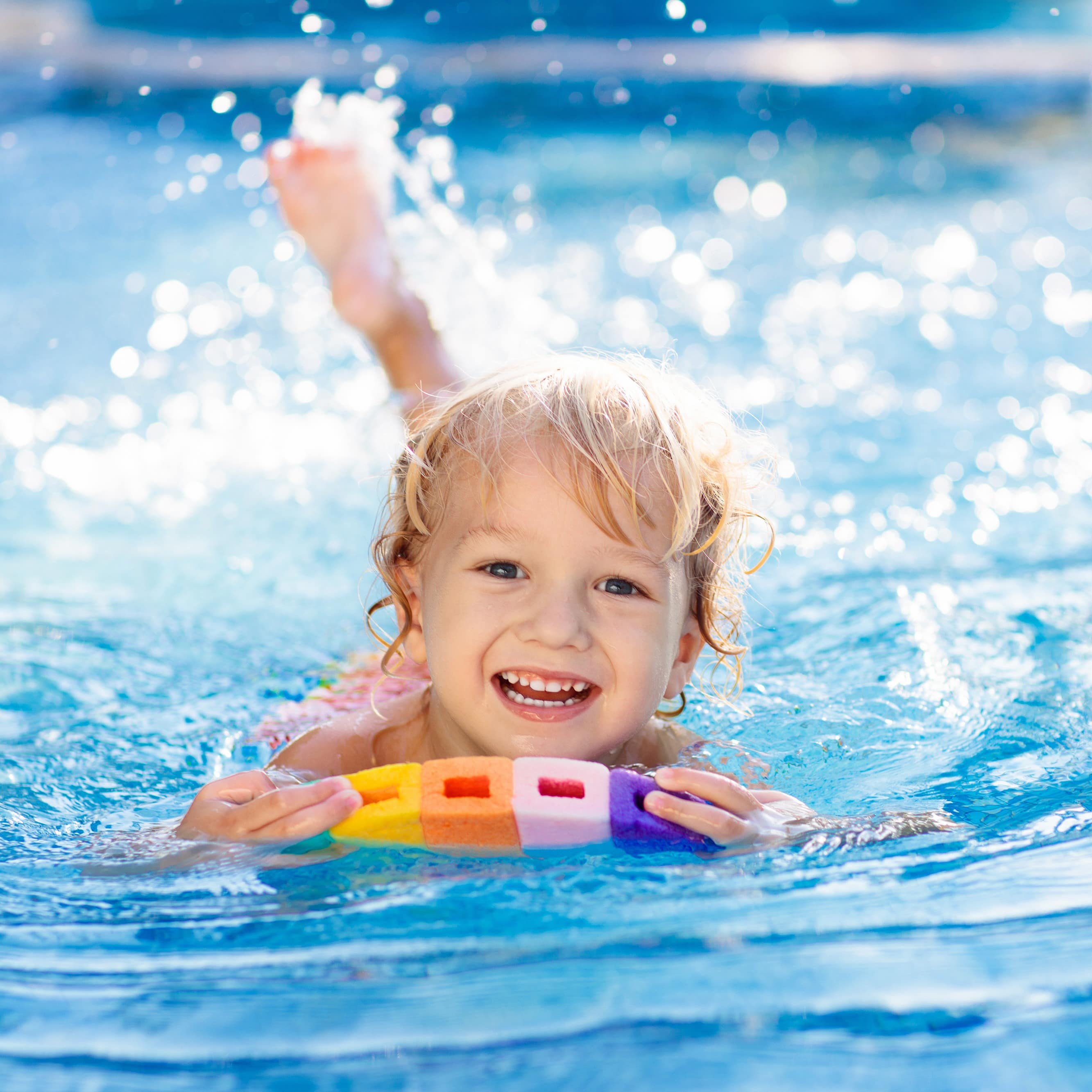 Kleines Kind paddelt auf einem bunten Board durch das Wasser.
