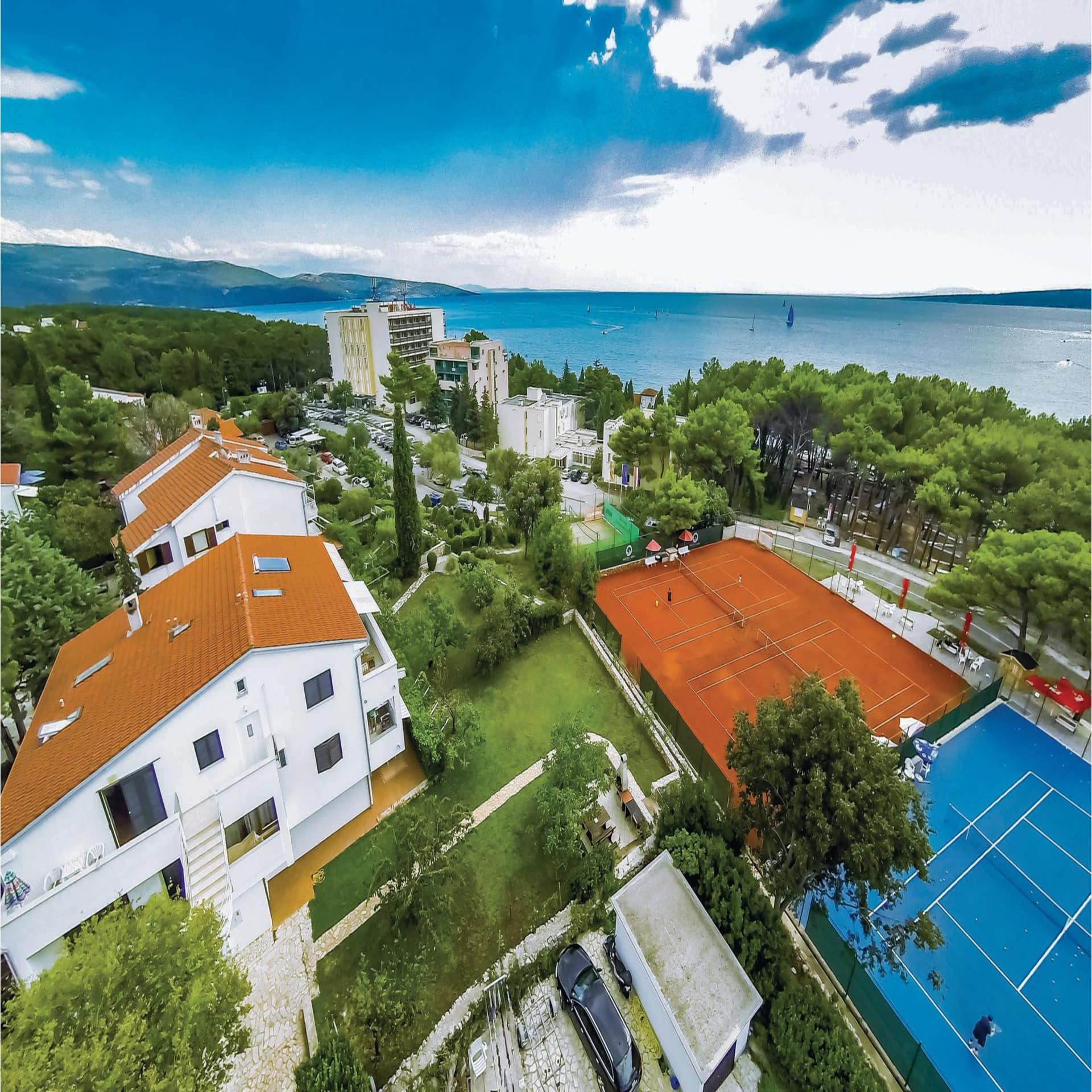 Blick von oben auf einen Ort am Meer und 2 Tennisplätze.