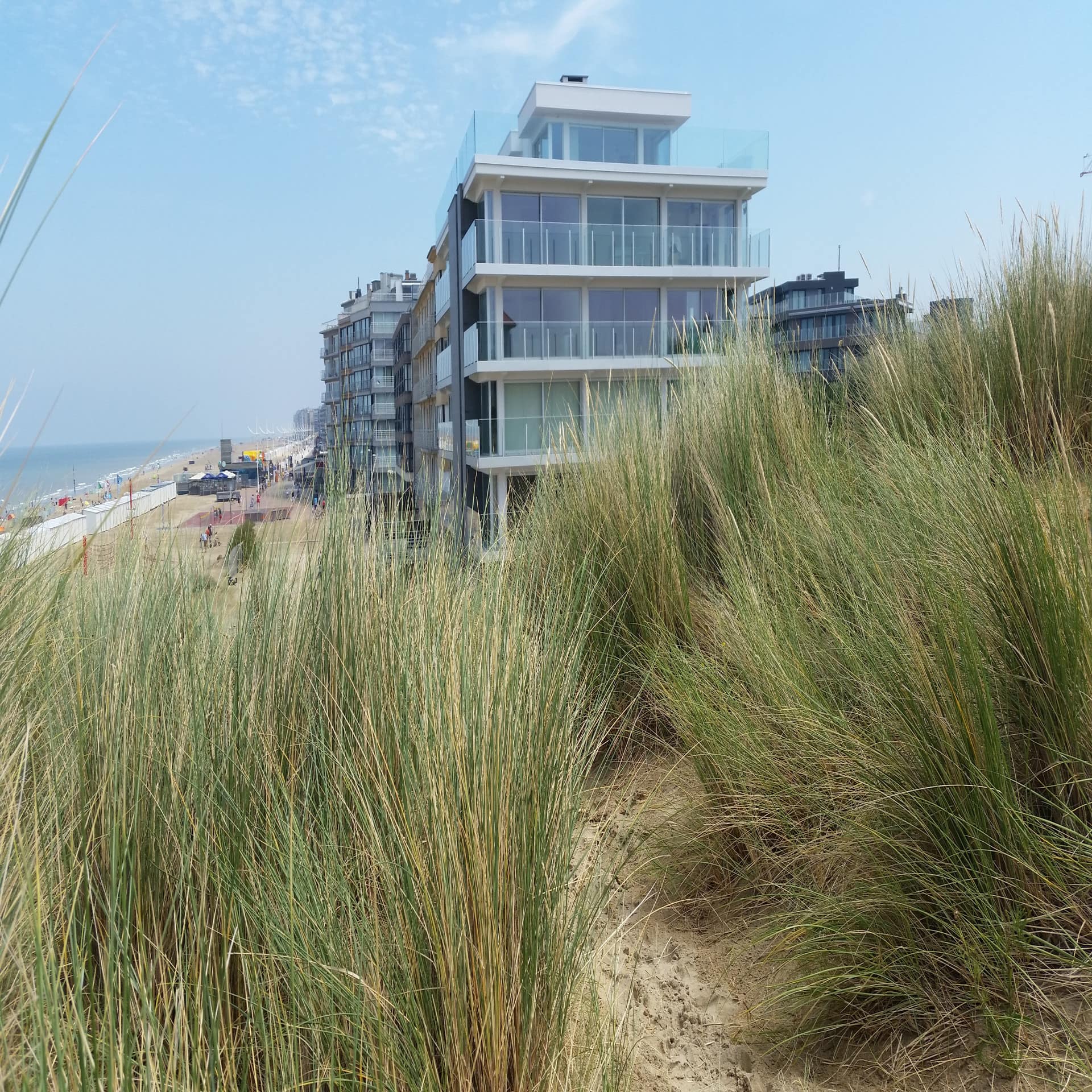 Blick durch das Dünengrad auf moderne Apartmenthäuser direkt am Strand.