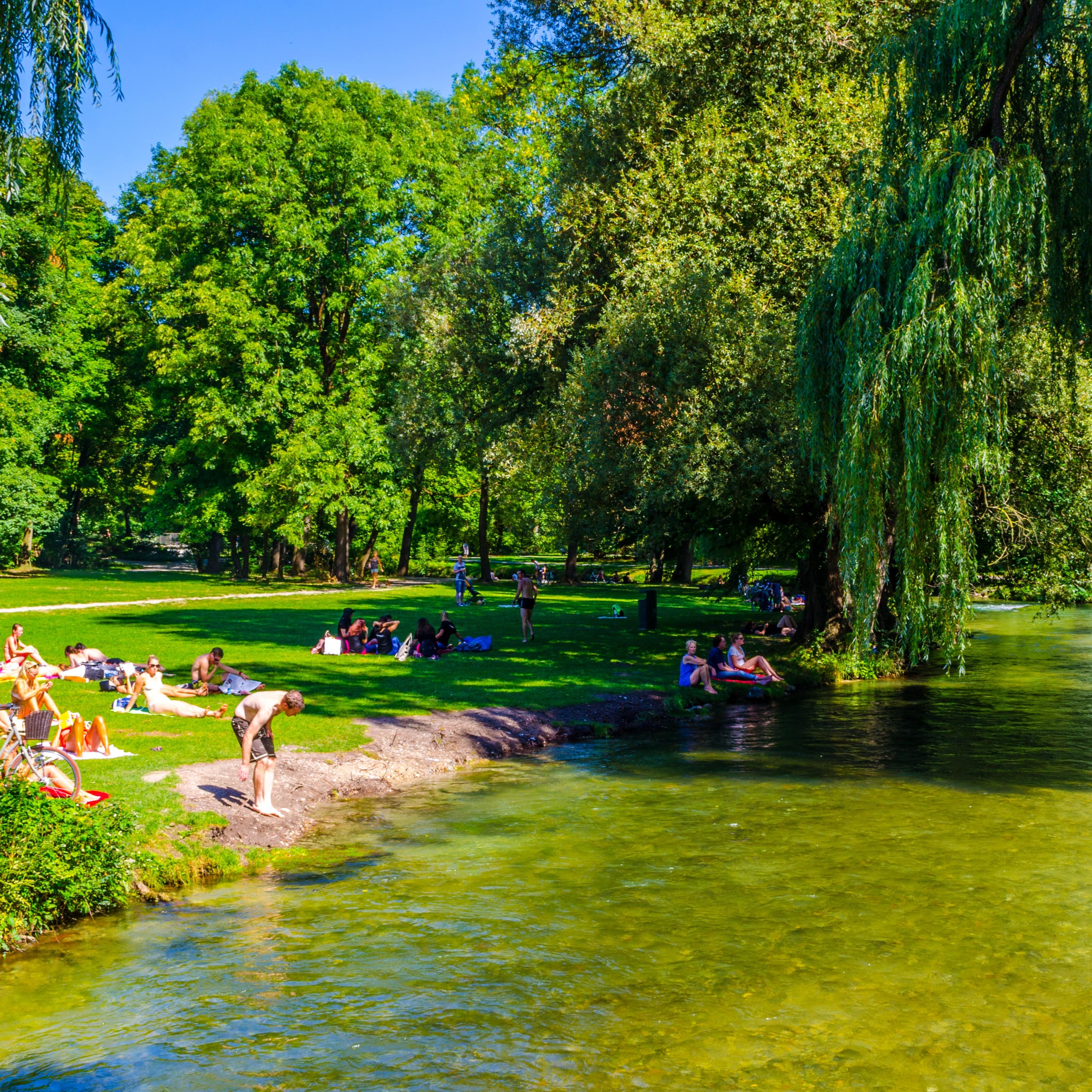 Leute liegen an einem Wasserlauf im Englischen Garten in der Sonne. 