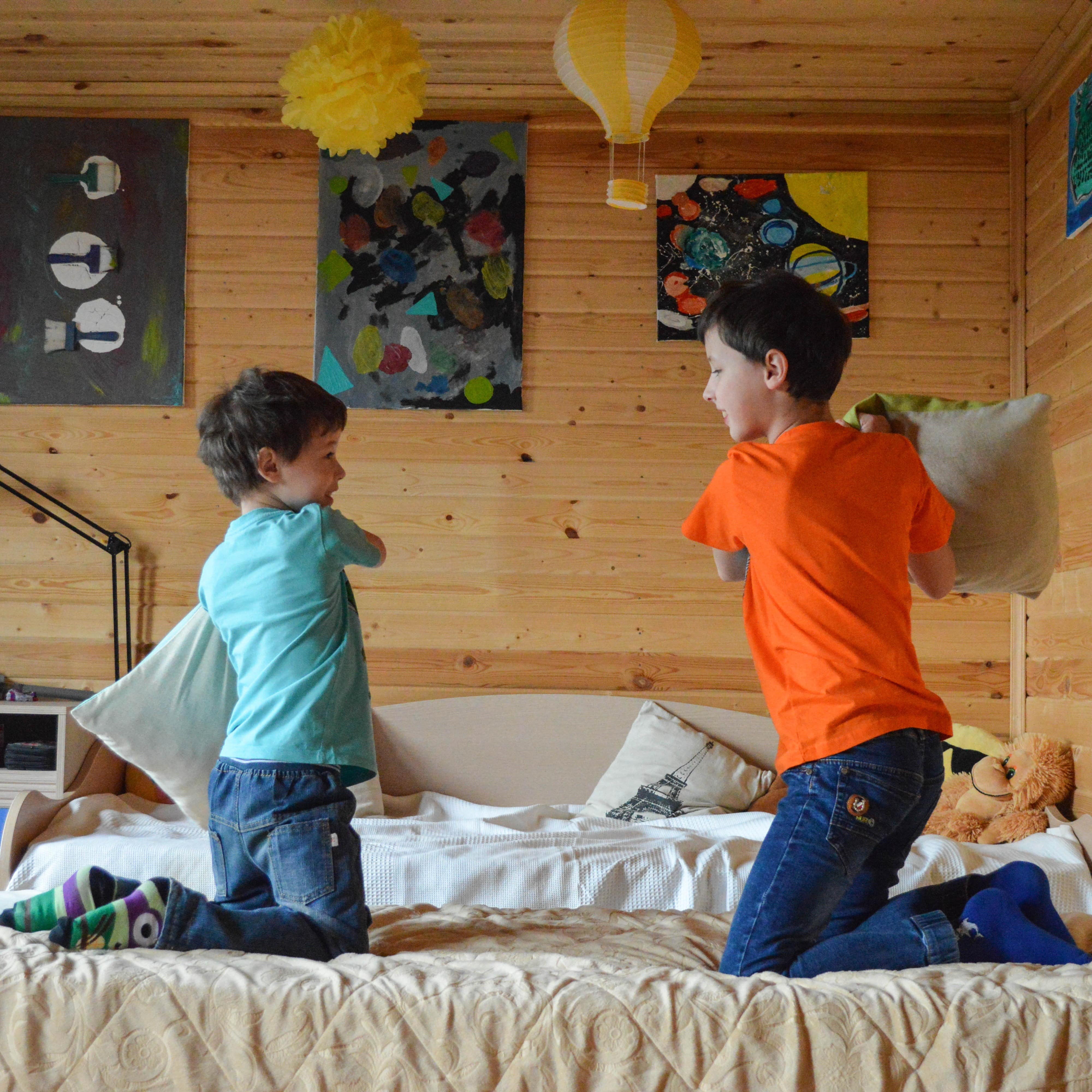 2 Jungs auf einem Bett machen eine Kissenschlacht.