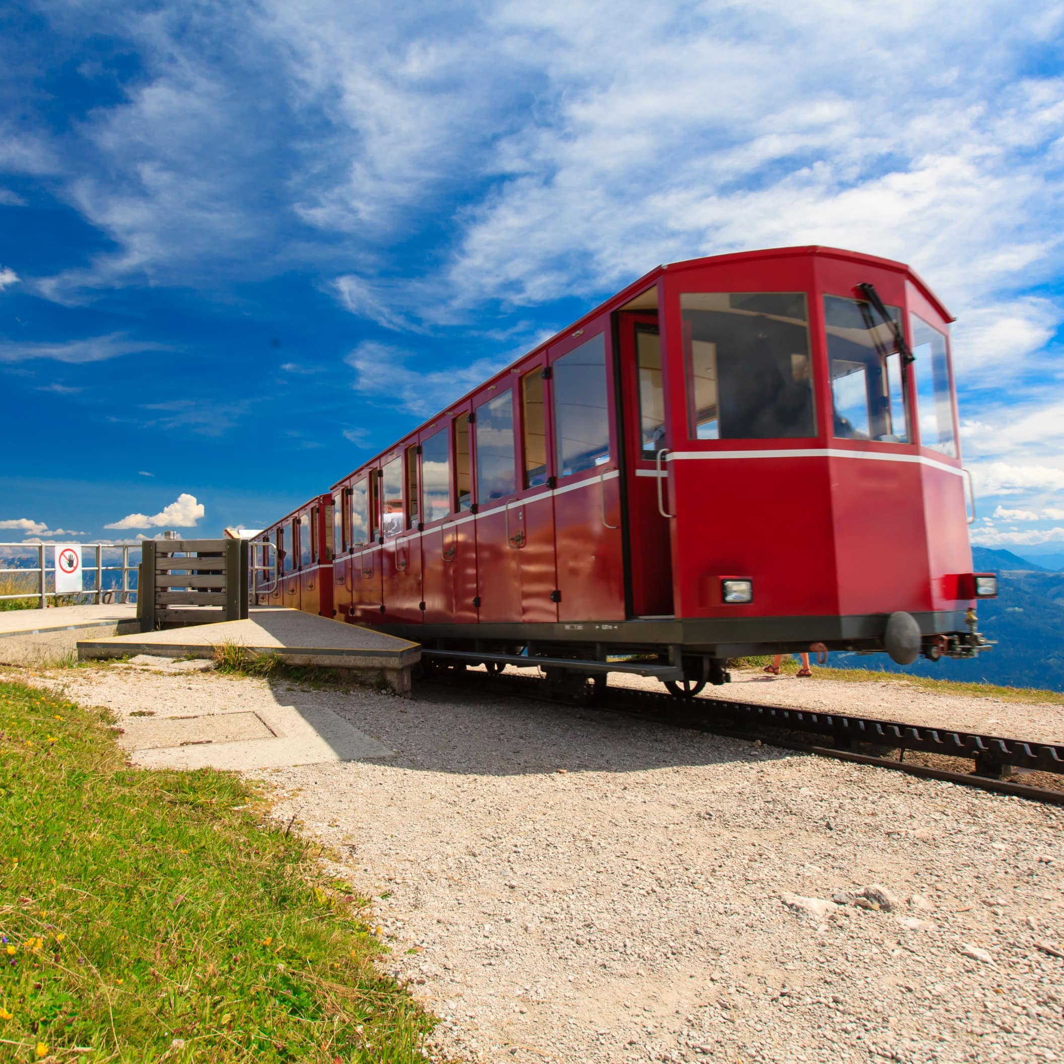 Eine rote Zahnradbahn in alpiner Landschaft bei Sonnenschein.