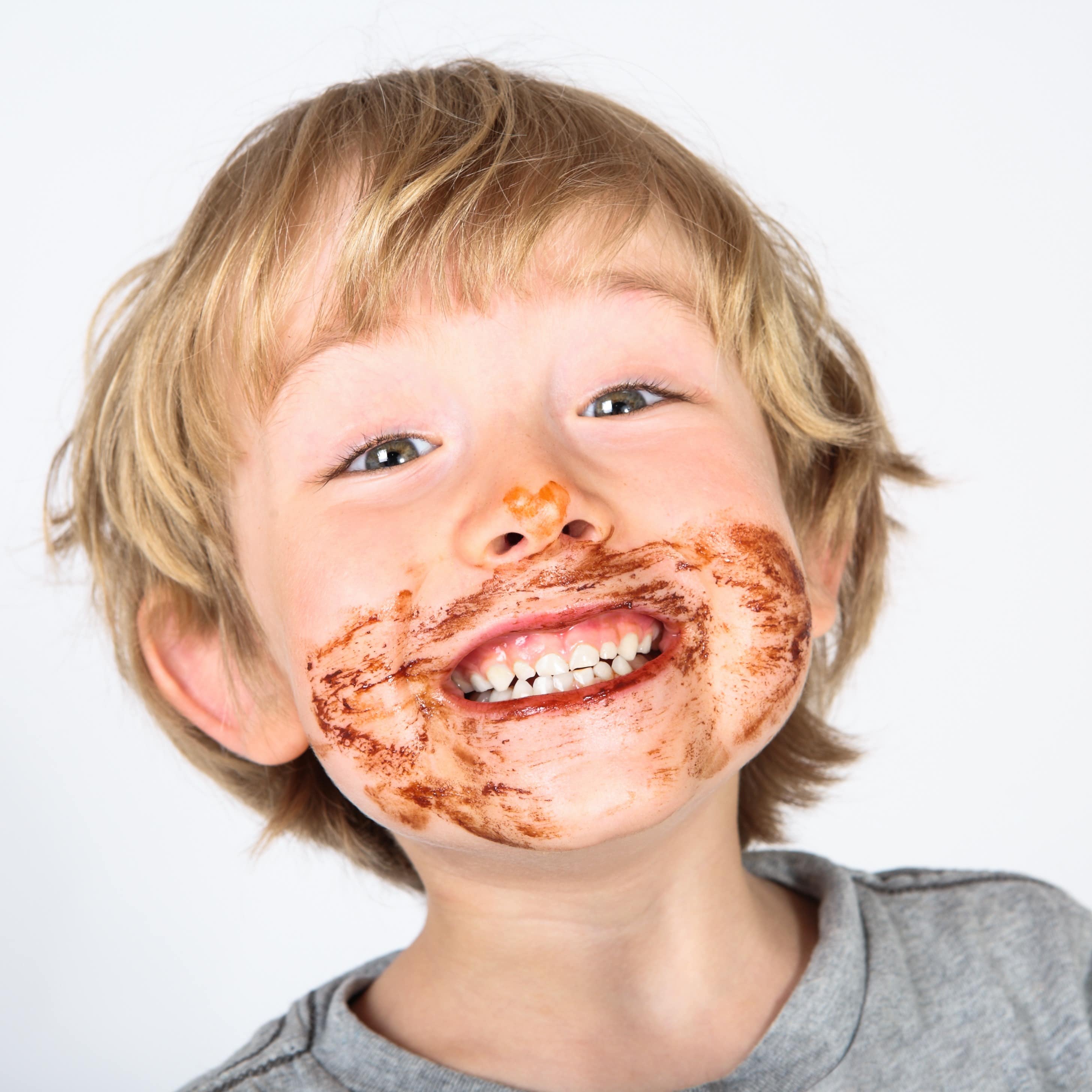 Blonder Junge mit Schokoladenverschmiertem Gesicht grinst in die Kamera.
