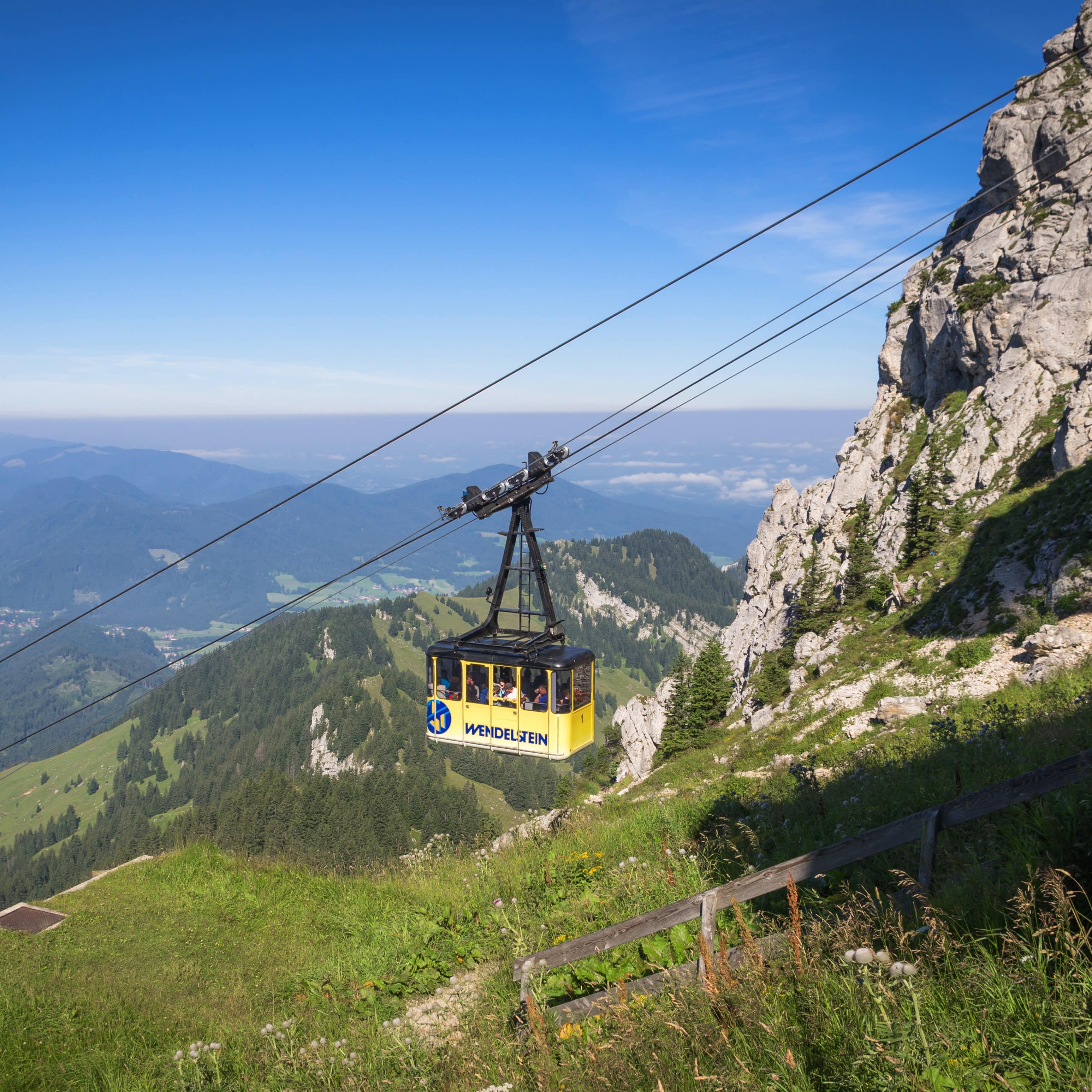 Die gelbe Kabine der Wendelstein Seilbahn vor einer Bergkulisse.