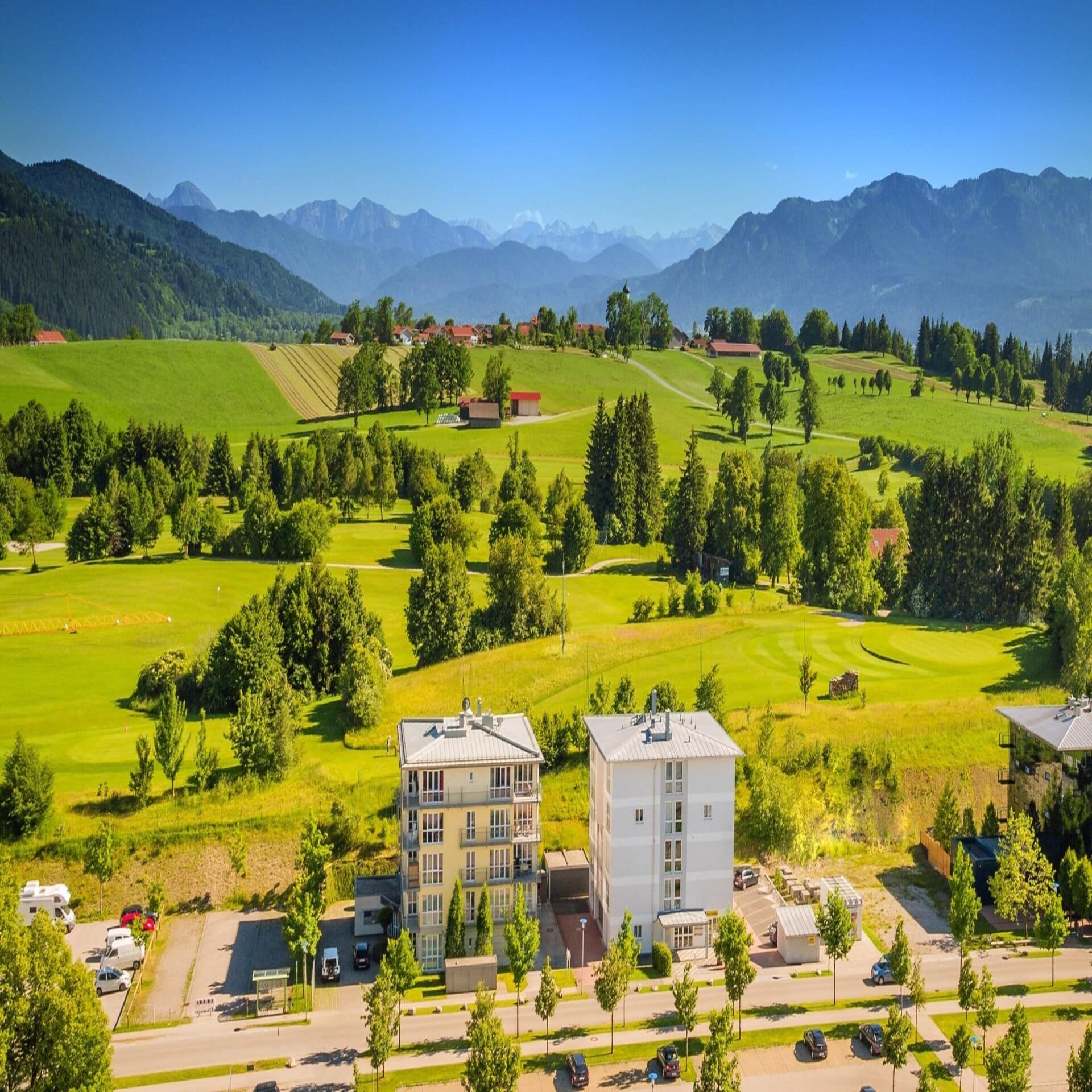 Blick von oben über die grüne Landschaft von Bad Tölz, 2 Gebäude sind im Vordergrund zu sehen.