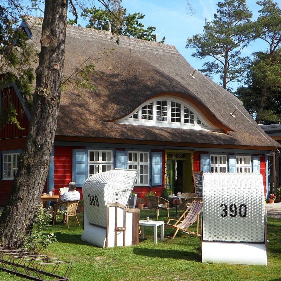 Haus mit Reetdach in Ostfriesland, im Garten stehen Strandkörbe und Sonnenliegen. 