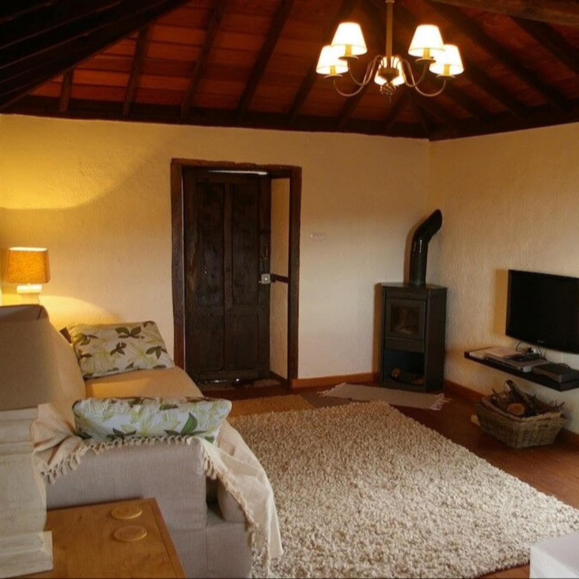Gemütlicher Wohnraum im Ferienhaus auf La Palma mit hellen Möbeln, dickem Teppich, Ofen und holzvertäfelter Decke