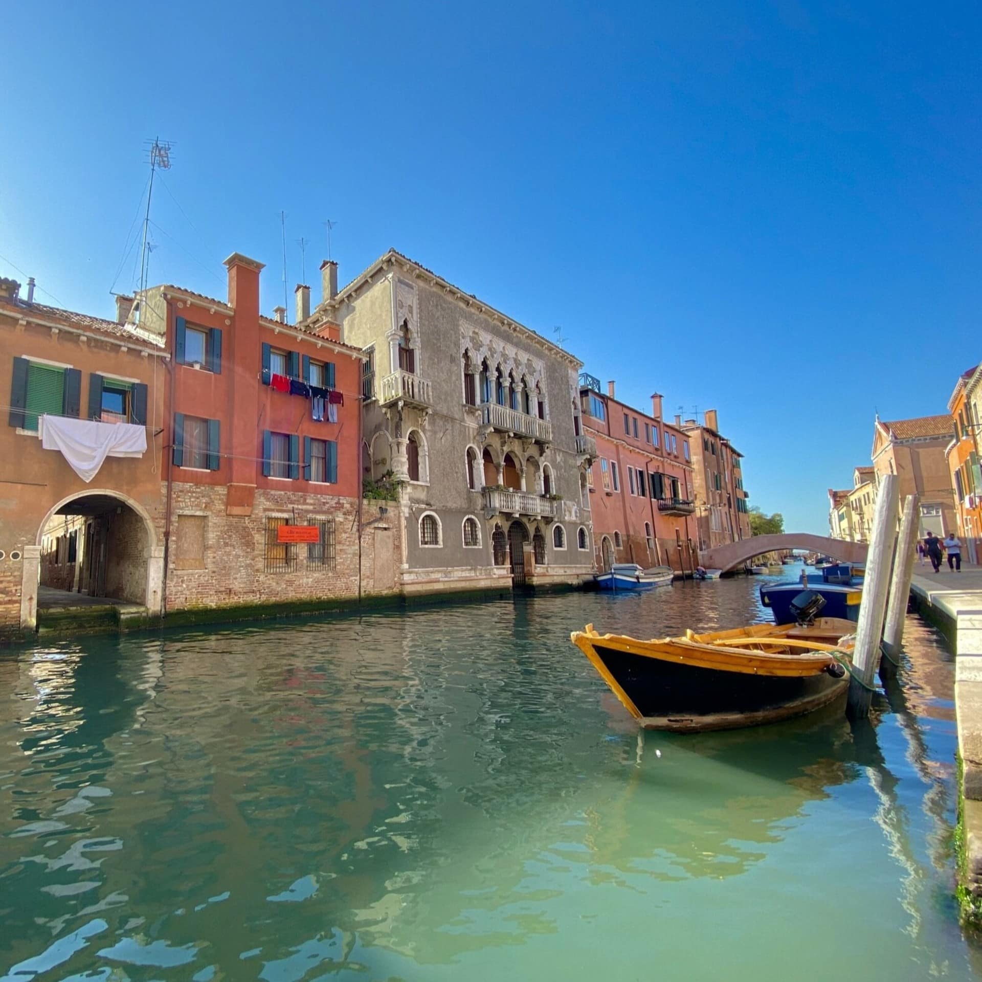 Häuser an einem Kanal in Venedig. Vorne ist eine Gondel zu sehen. Die Sonne scheint. 