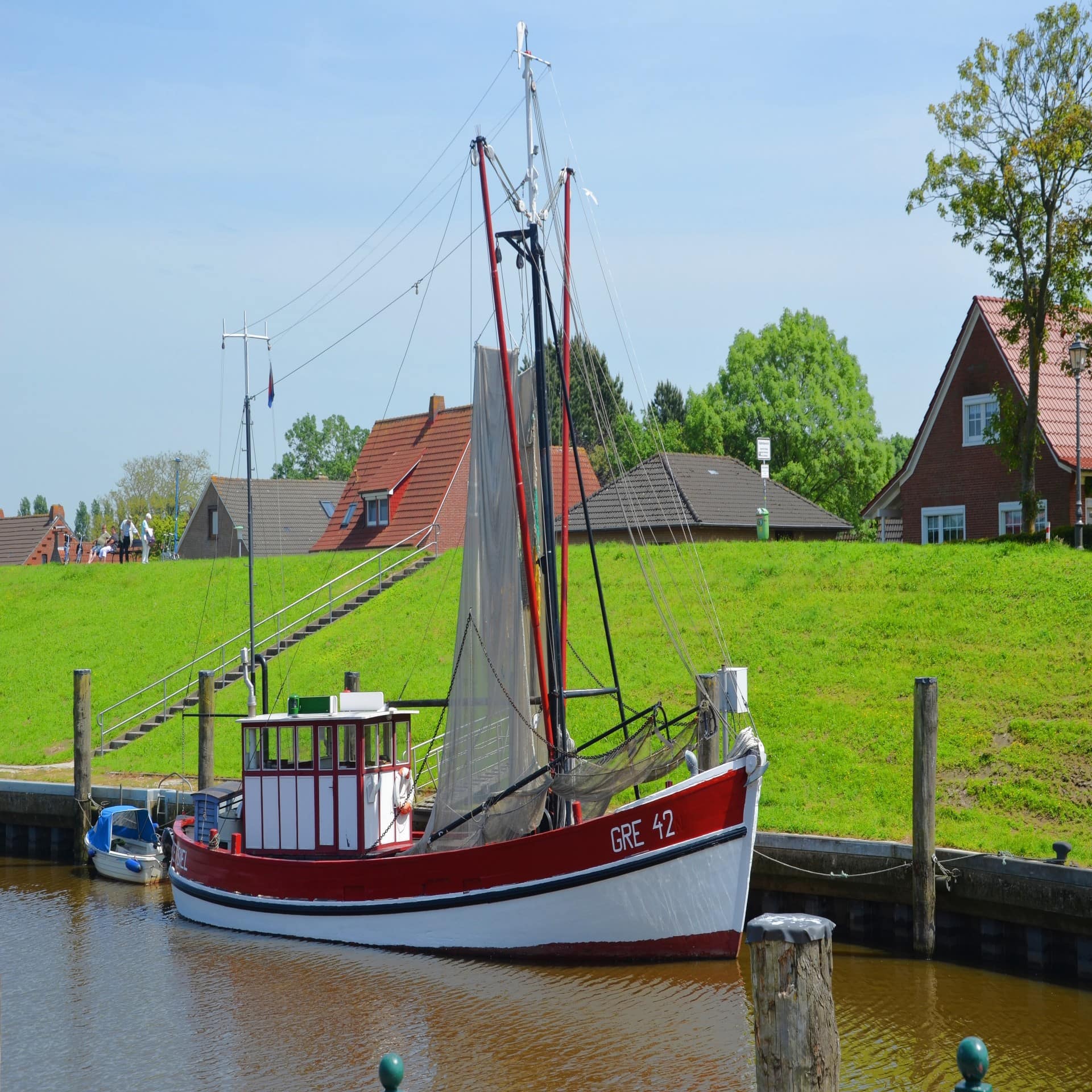 Blick auf ein kleines Fischerboot vor den Deich, dahinter sind Häuser zu sehen. 