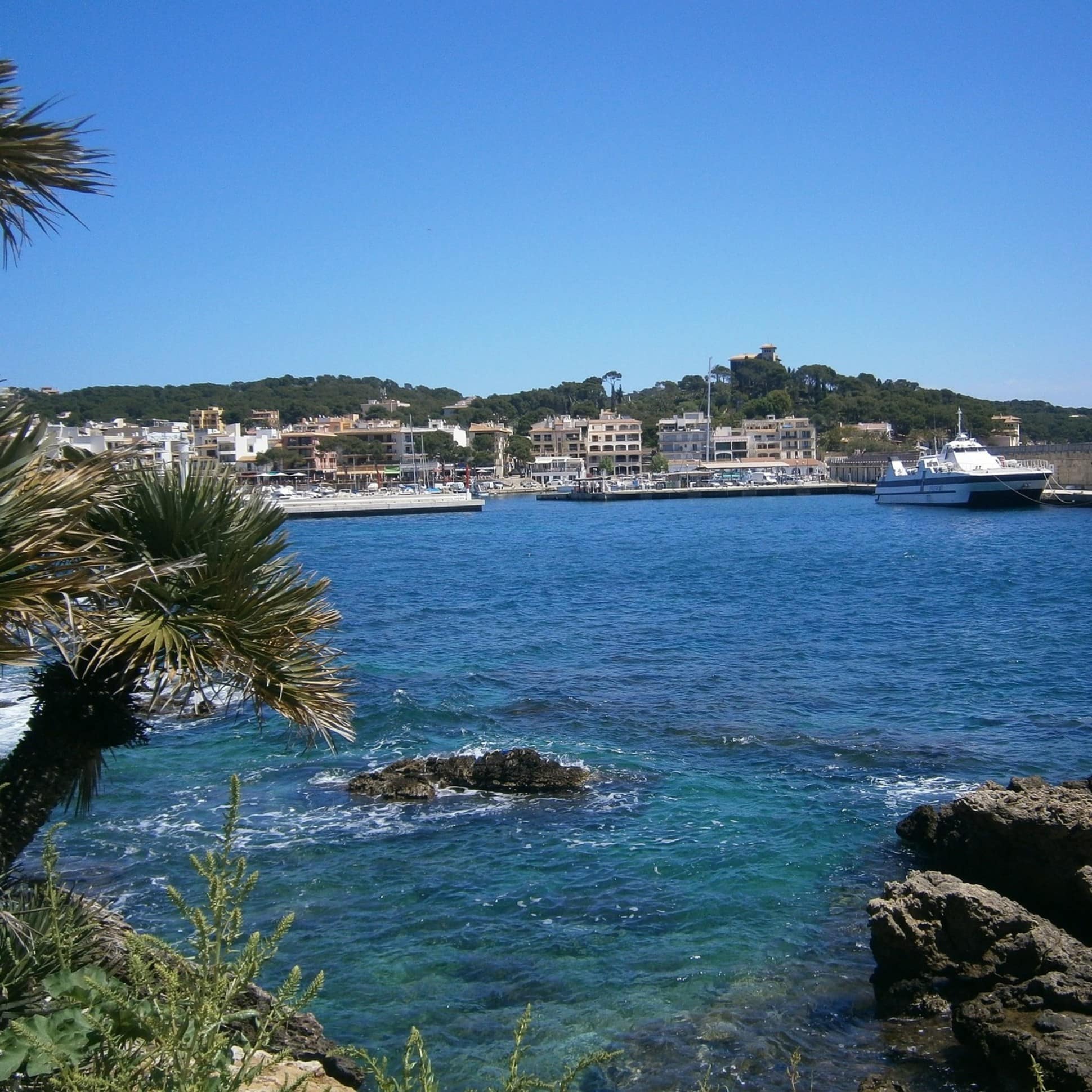 Blick über das Wasser auf den Hafen von Cala Ratjada mit Häusern im Hintergrund