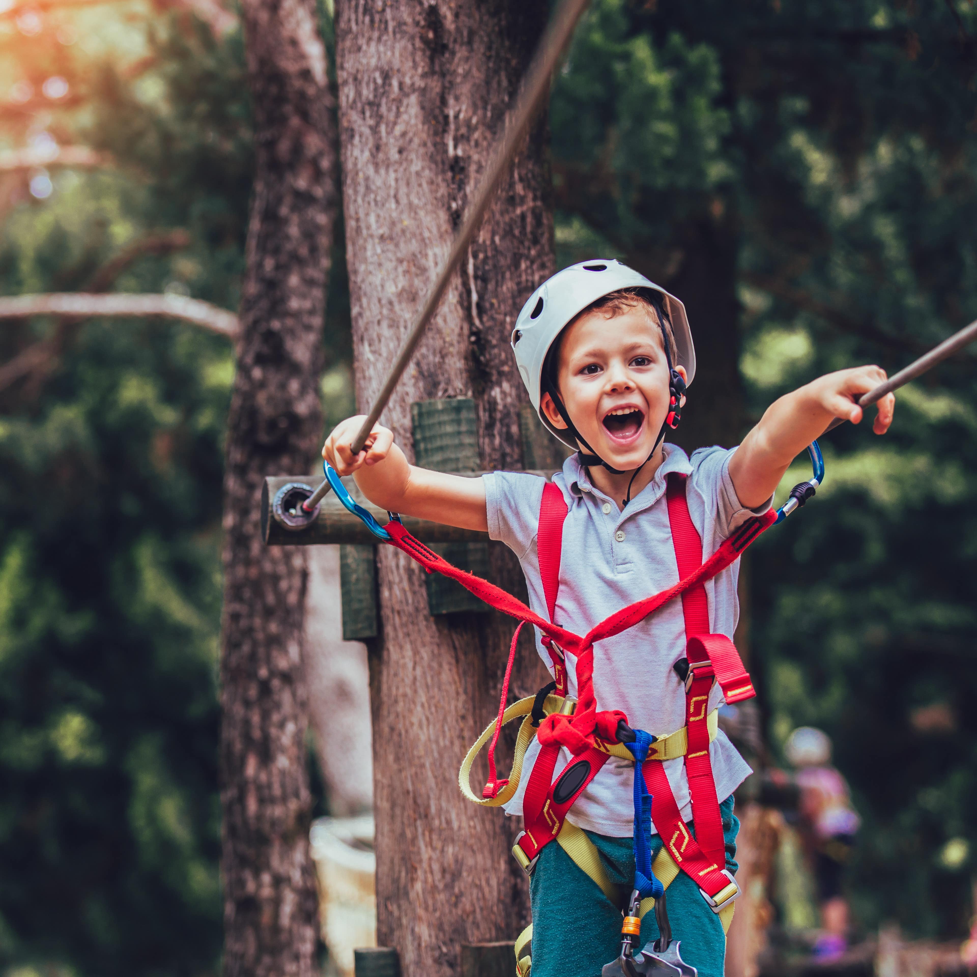 Ein Junge in Kletterausrüstung und mit Helm auf einem Parcours im Kletterpark.