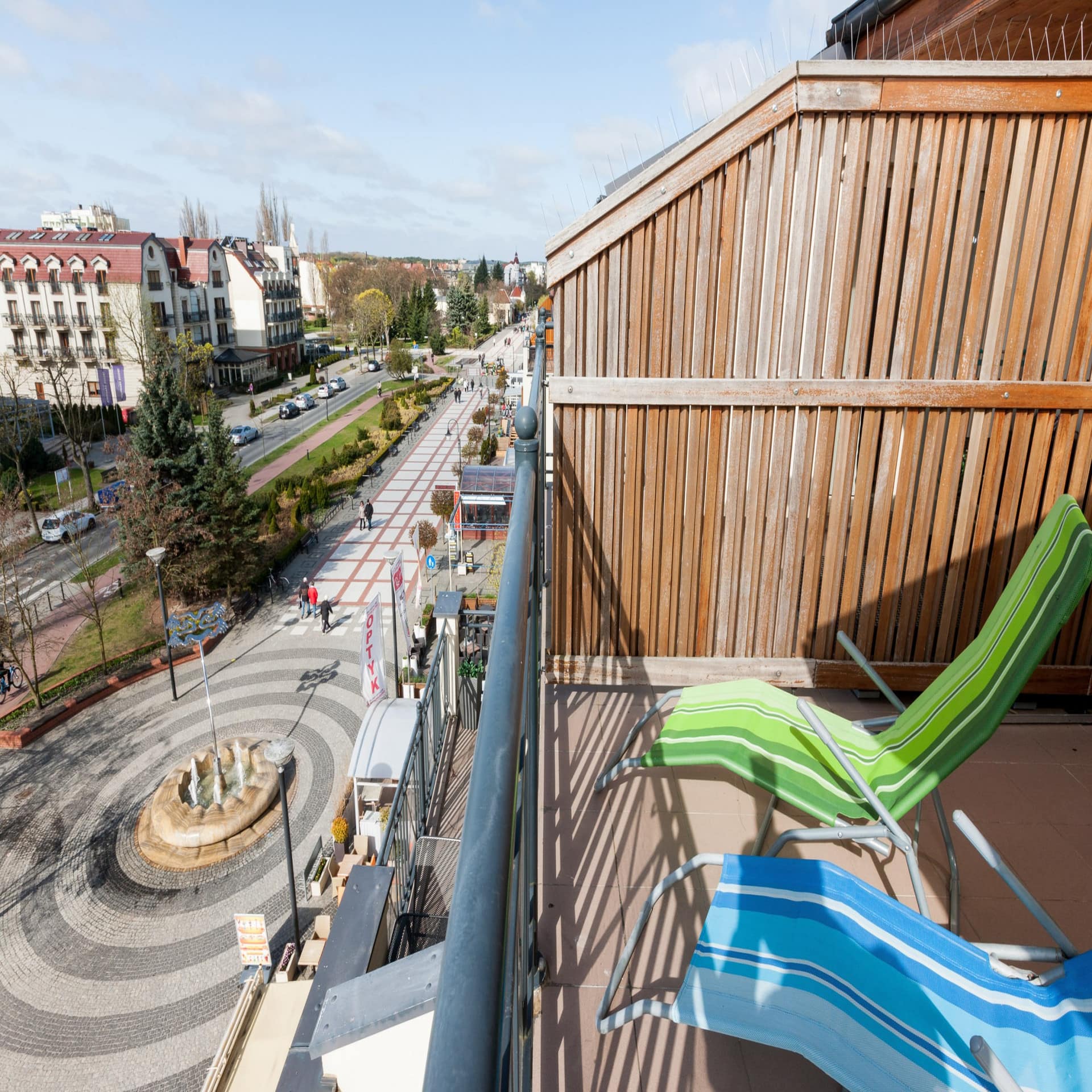 Blick vom Balkon mit Sonnenliegen auf die Innenstadt und einen Springbrunnen. 