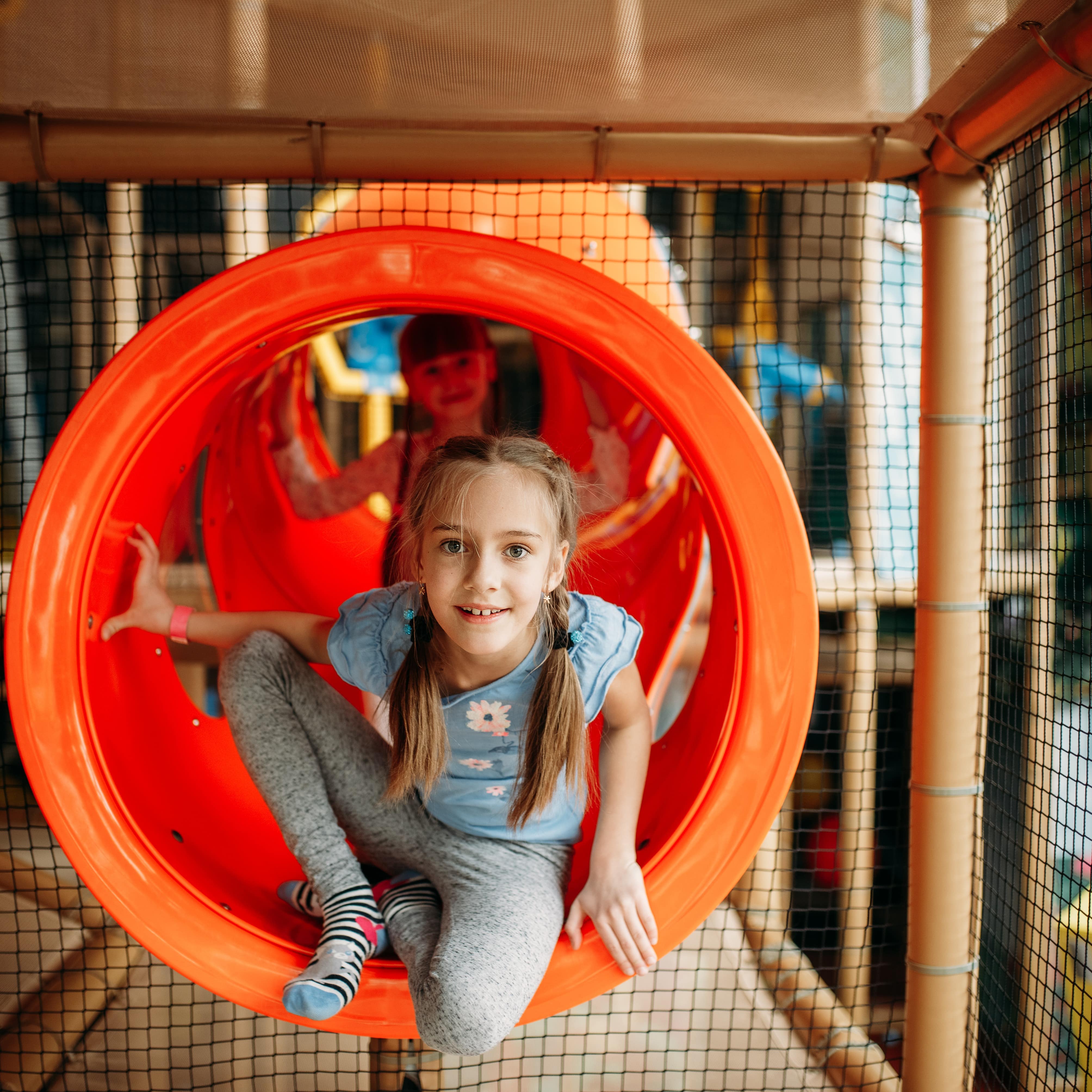2 Mädchen in einer Röhre in einem Kletterlabyrinth.