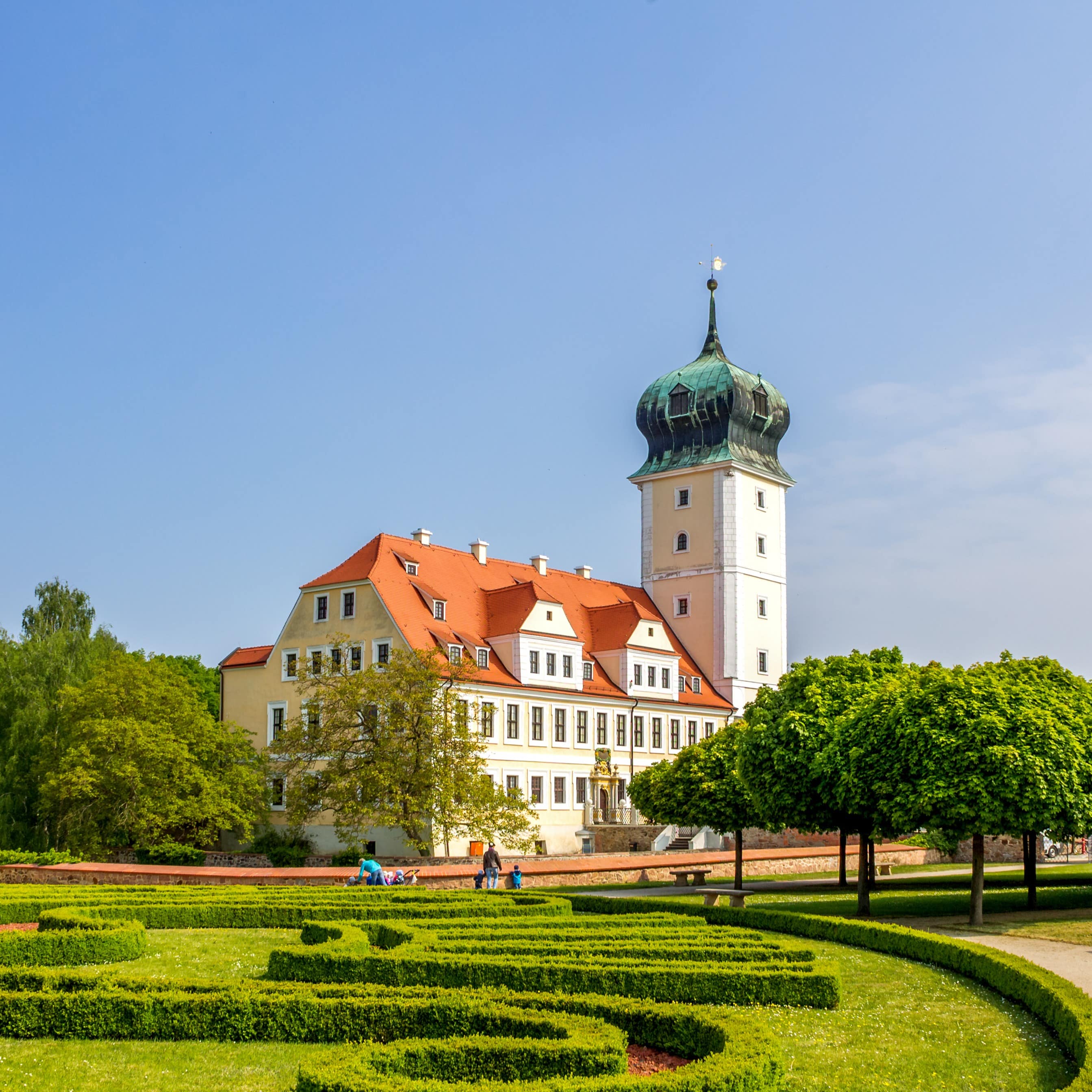 Blick auf das Barockschloss Delitzsch und den Garten davor. Eltern mit Kindern sind vor dem Schloss zu erkennen.