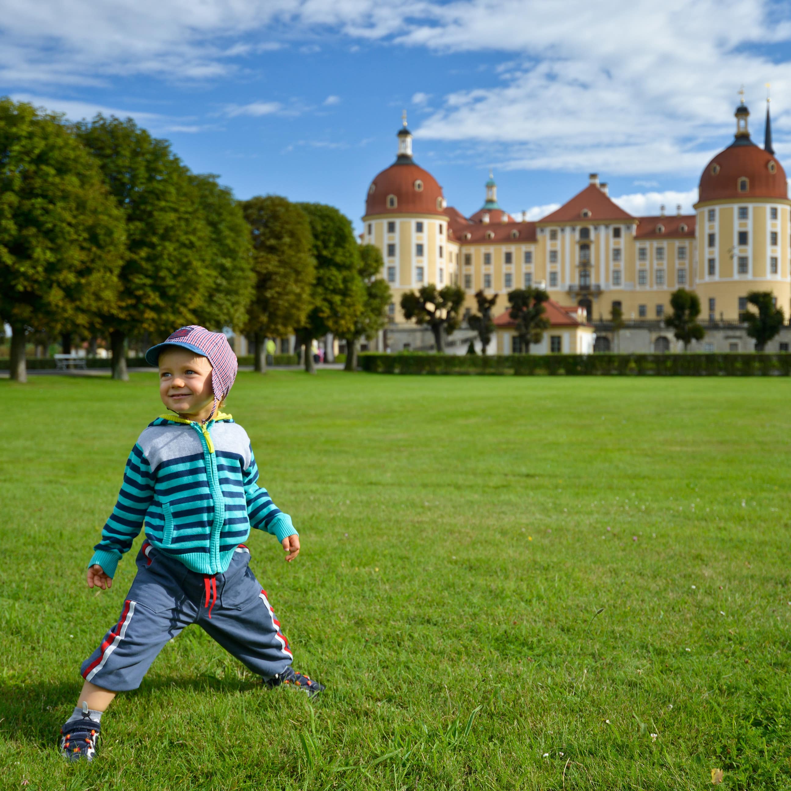 Kleiner Junge in eklektischer Kleidung auf der grünen Wiese vor Schloss Moritzburg.