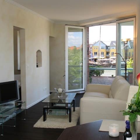 Wohnzimmer einer exklusiven Ferienwohnung mit Blick auf den Hafen und Balkon