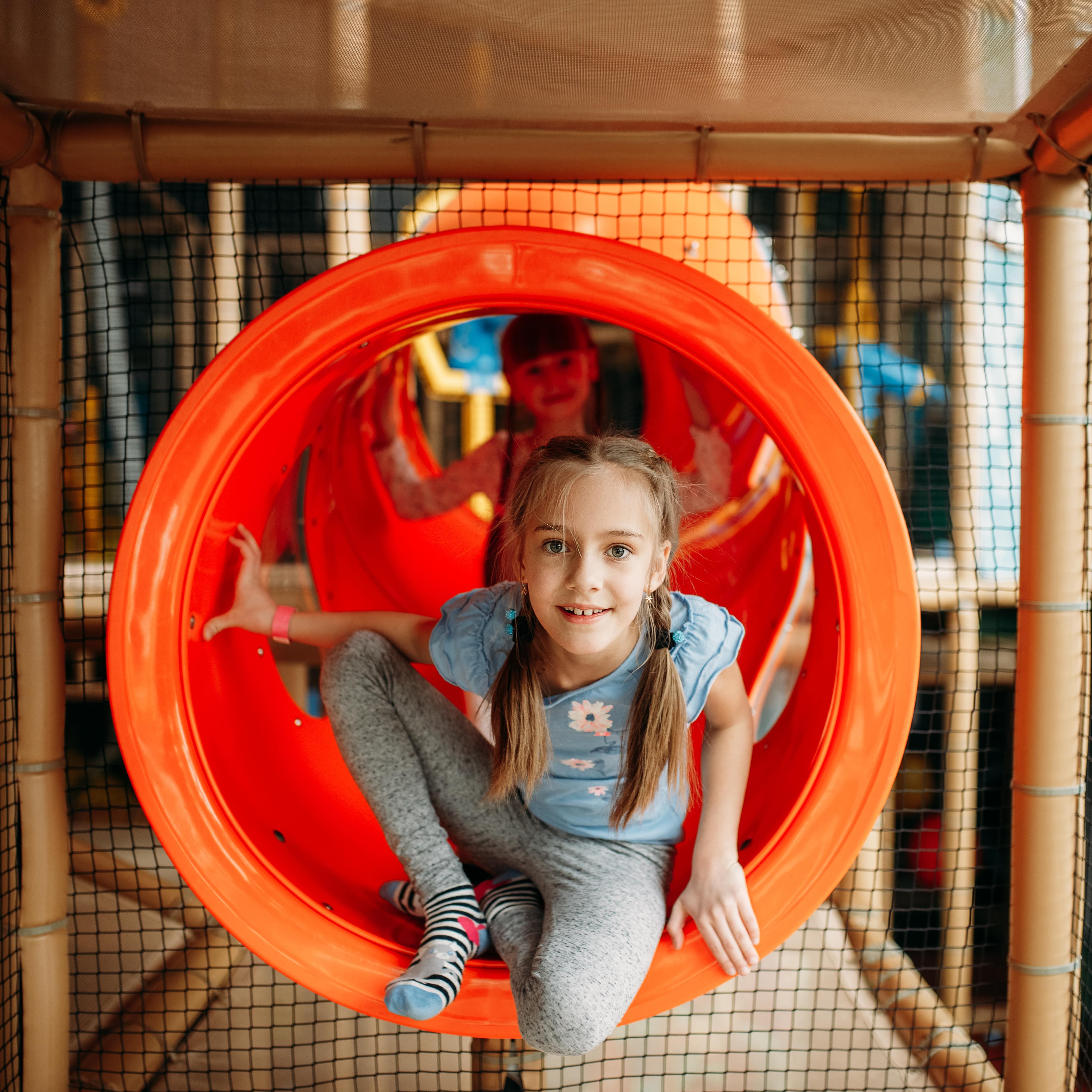 Ein Mädchen klettert aus einem orangenen Tunnel in einem Indoor Spielplatz.