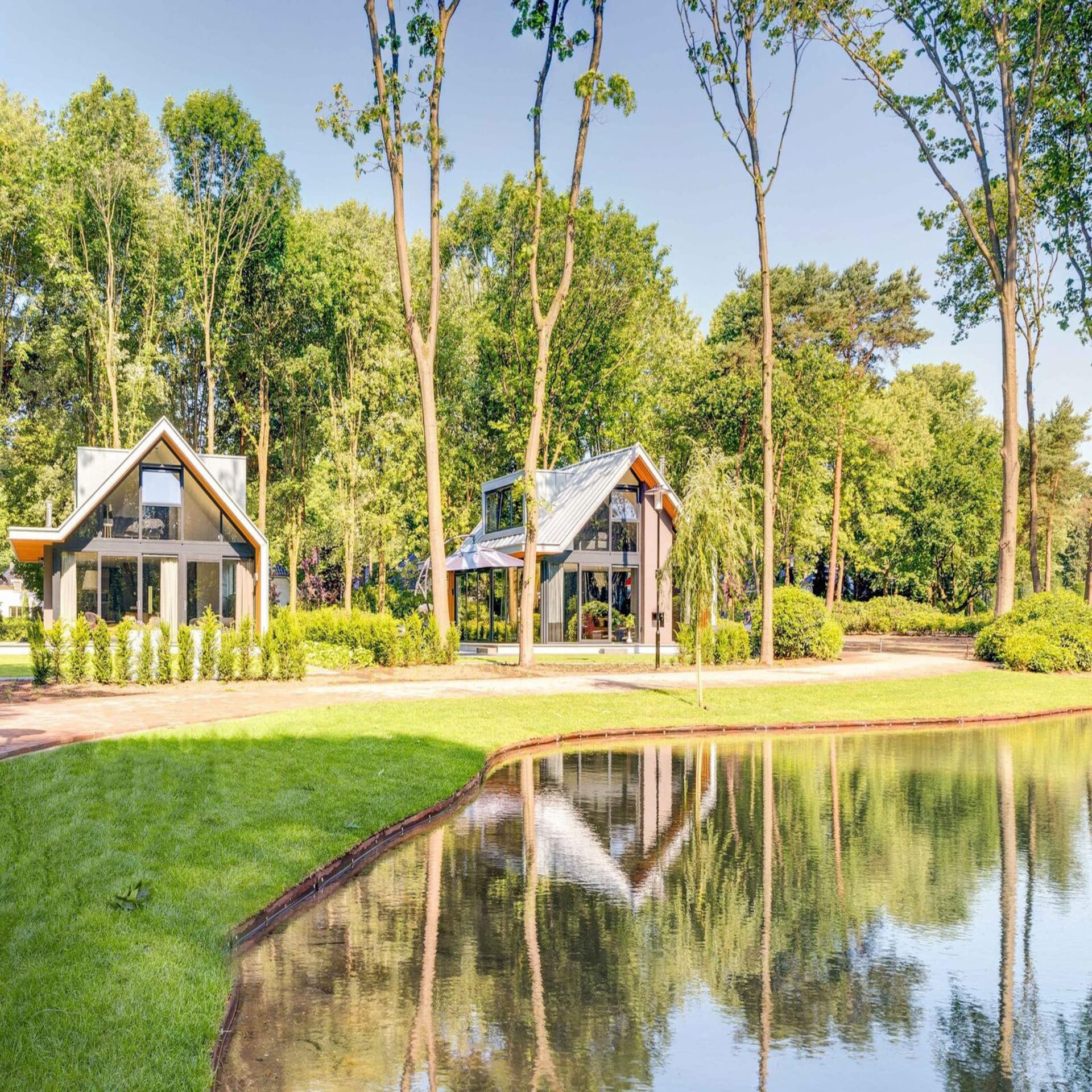 Moderne Häuschen mit viel Glas in einem parkähnlichen Ferienpark mit einem See.