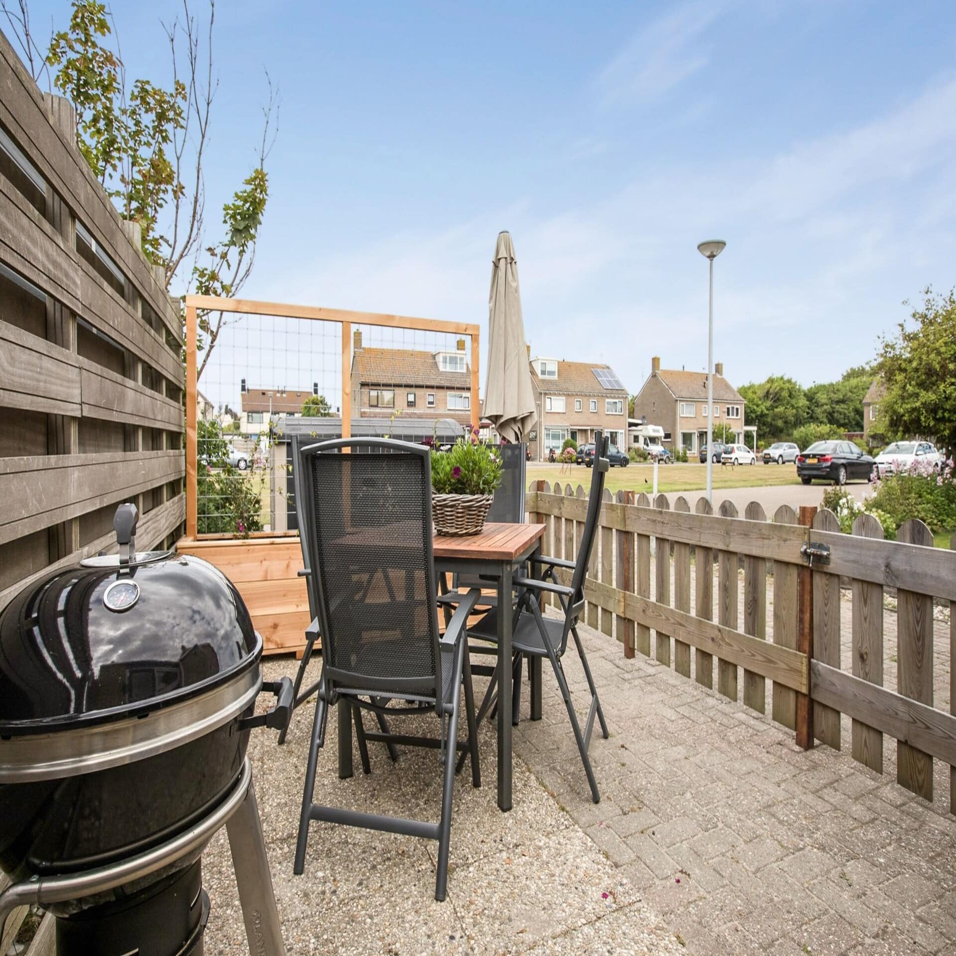 Kleine Terrasse mit Grill und Sitzgelegenheiten und Blick auf Häuser.