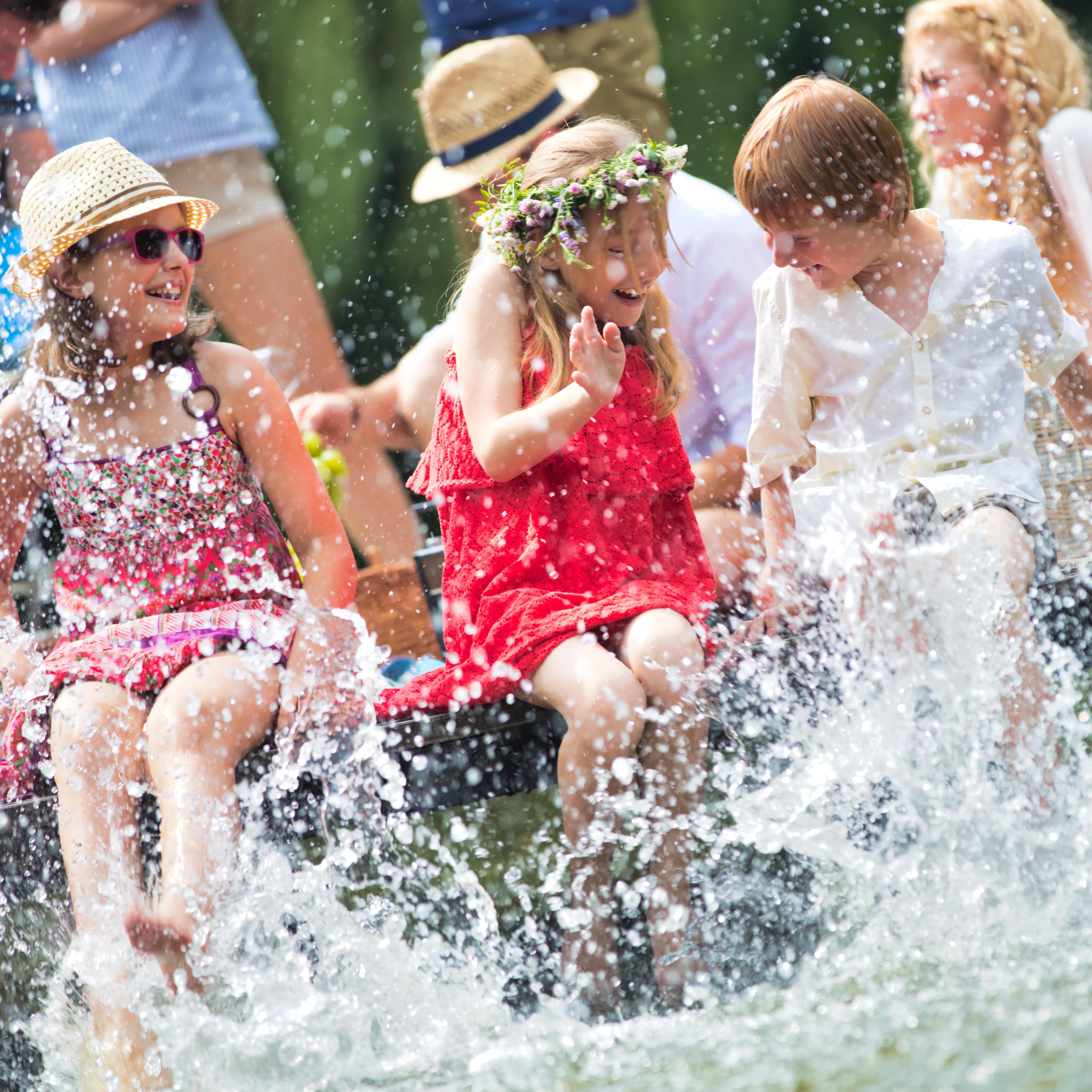 Mutter und 2 Kinder sitzen auf einem Holzsteg und spritzen mit den Beinen im Wasser.
