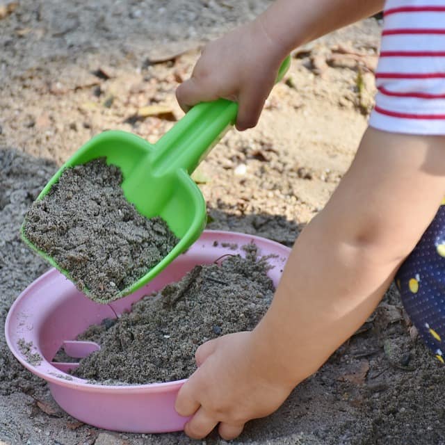 Arme eines kleinen Kindes mit Sandspielzeug in einer Sandkiste