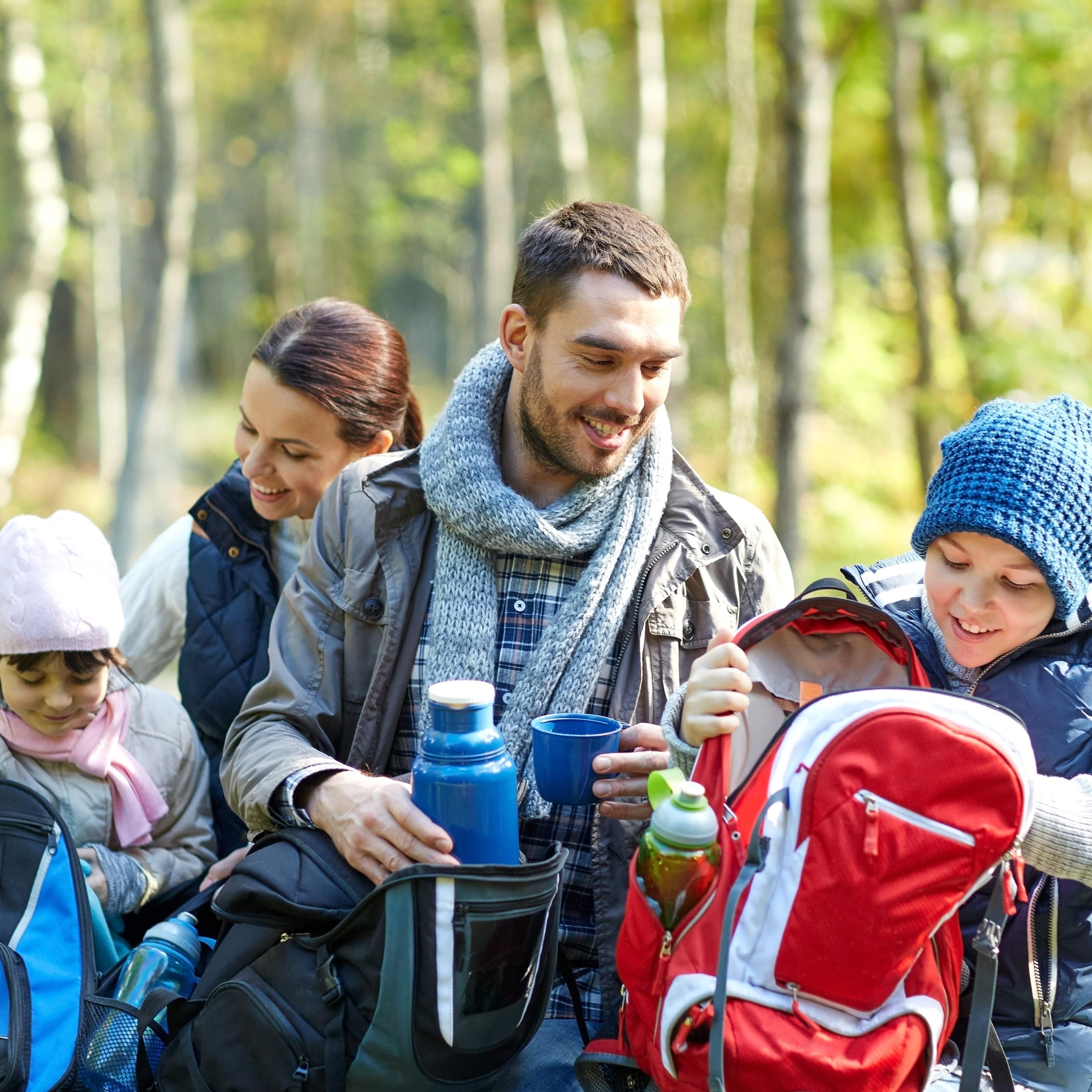 Familie mit 2 Kindern machen eine Pause auf einer Wanderung und holen Essen und Getränke aus den Rucksäcken.