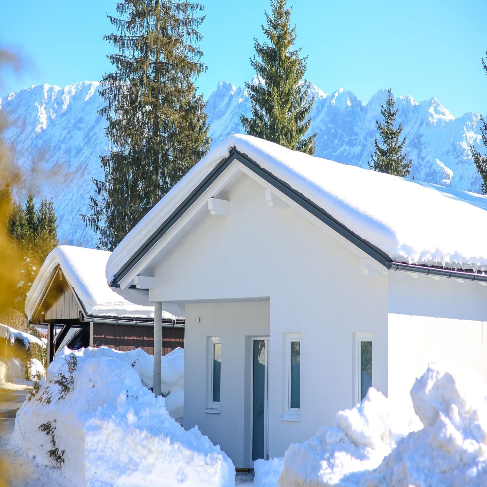 Kleine verschneite Häuschen. Im Hintergrund die Berge. Die Sonne scheint.