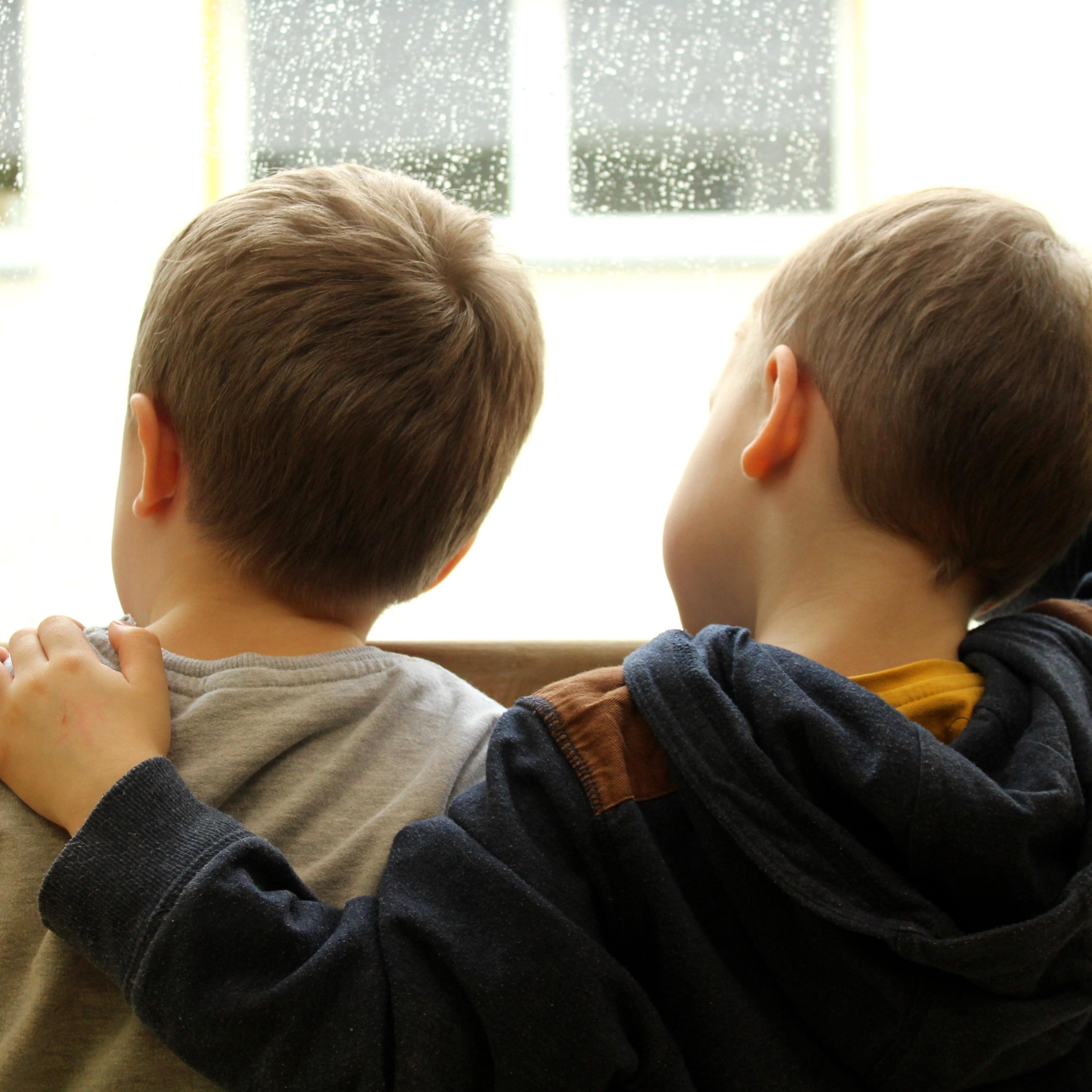Zwei Jungen vor einer nassgeregneten Fensterscheibe